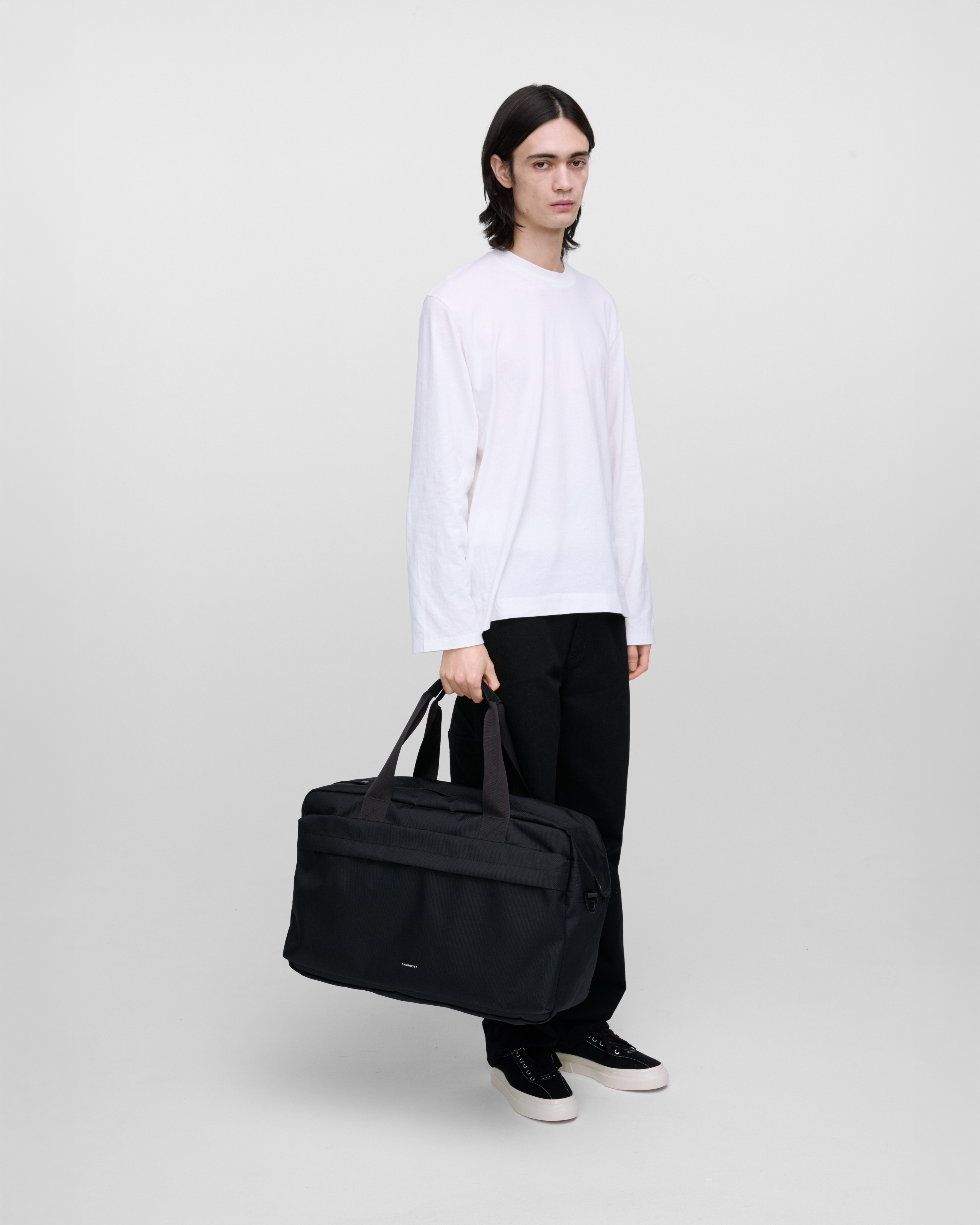 Male model holding Sandqvist GO Weekender L, black. Front view, holding the bag in one hand.