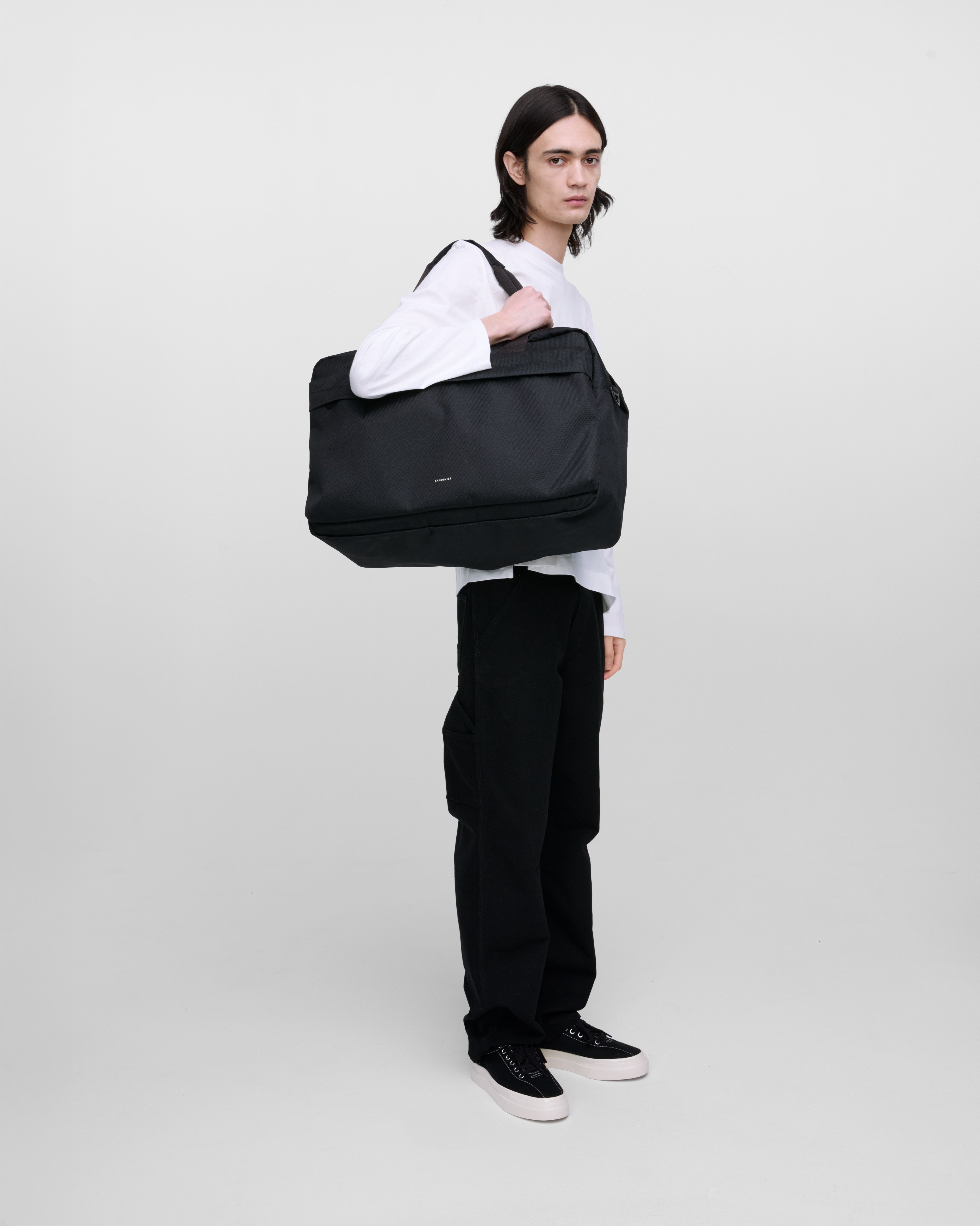 Male model wearing Sandqvist GO Weekender L, black. Side view, wearing the bag on one shoulder.