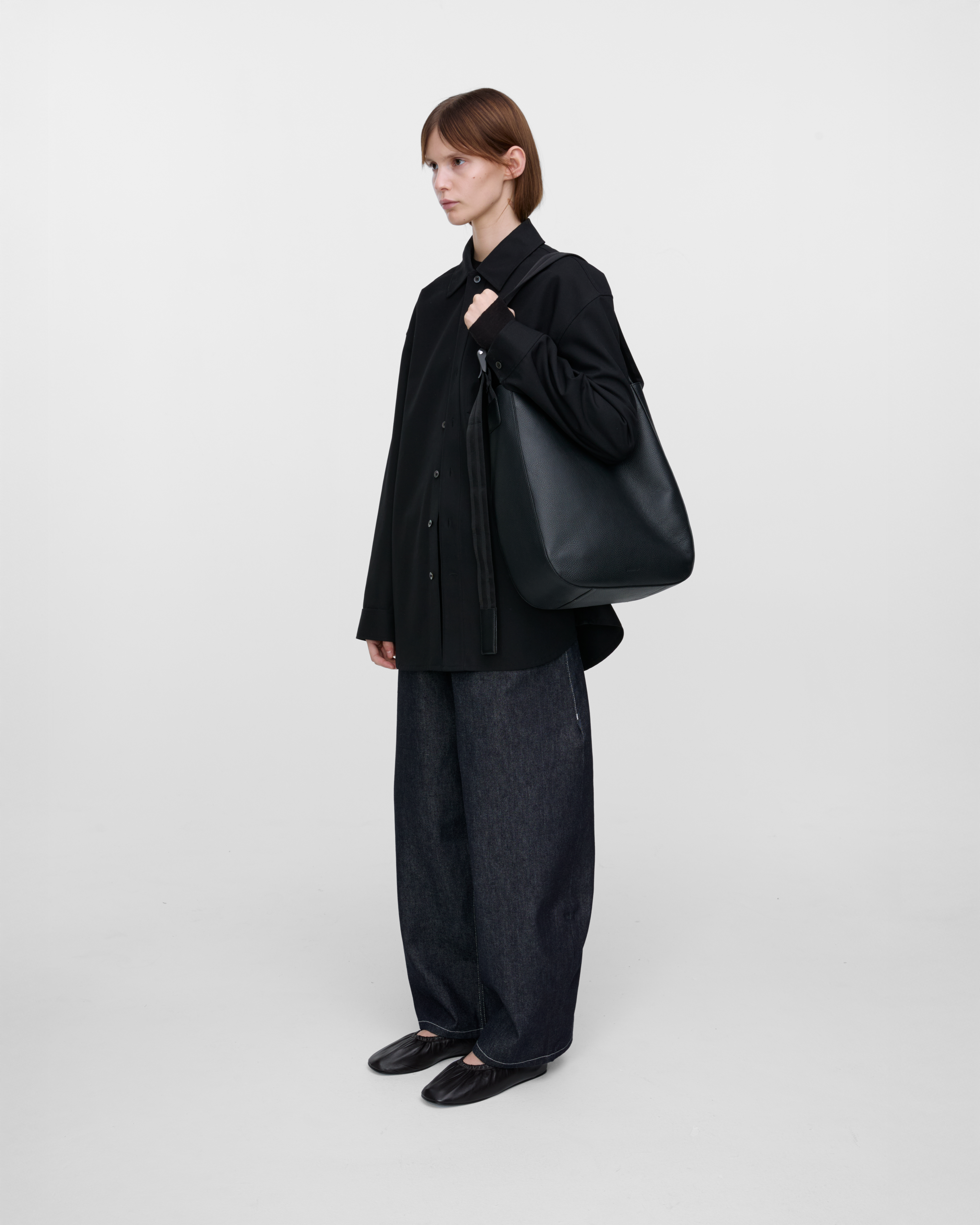 Female model wearing Sandqvist Agile Hobo Tote Bag, black. Side view, wearing the bag on one shoulder.