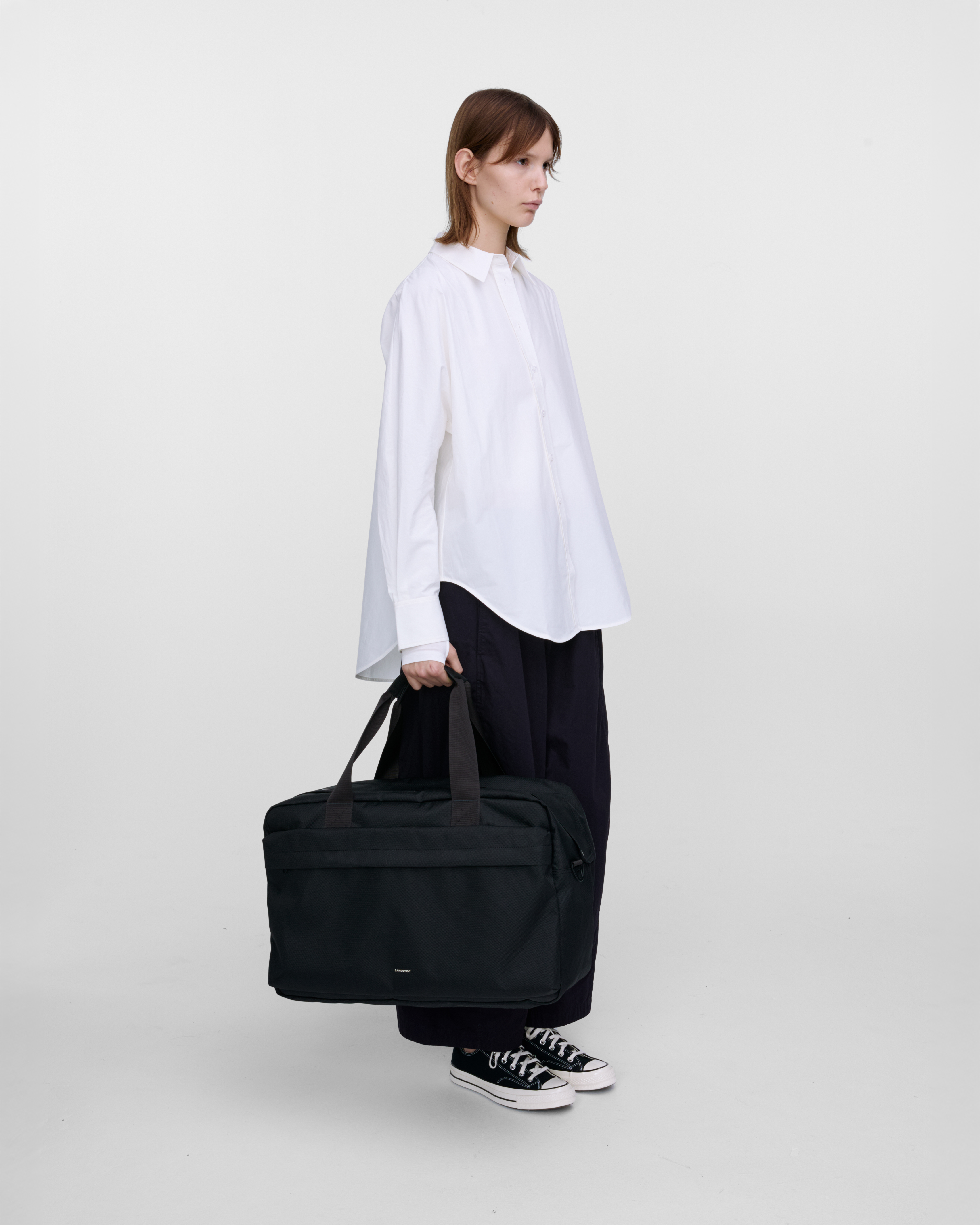 Female model holding Sandqvist GO Weekender L, black. Side view, holding the bag in one hand.