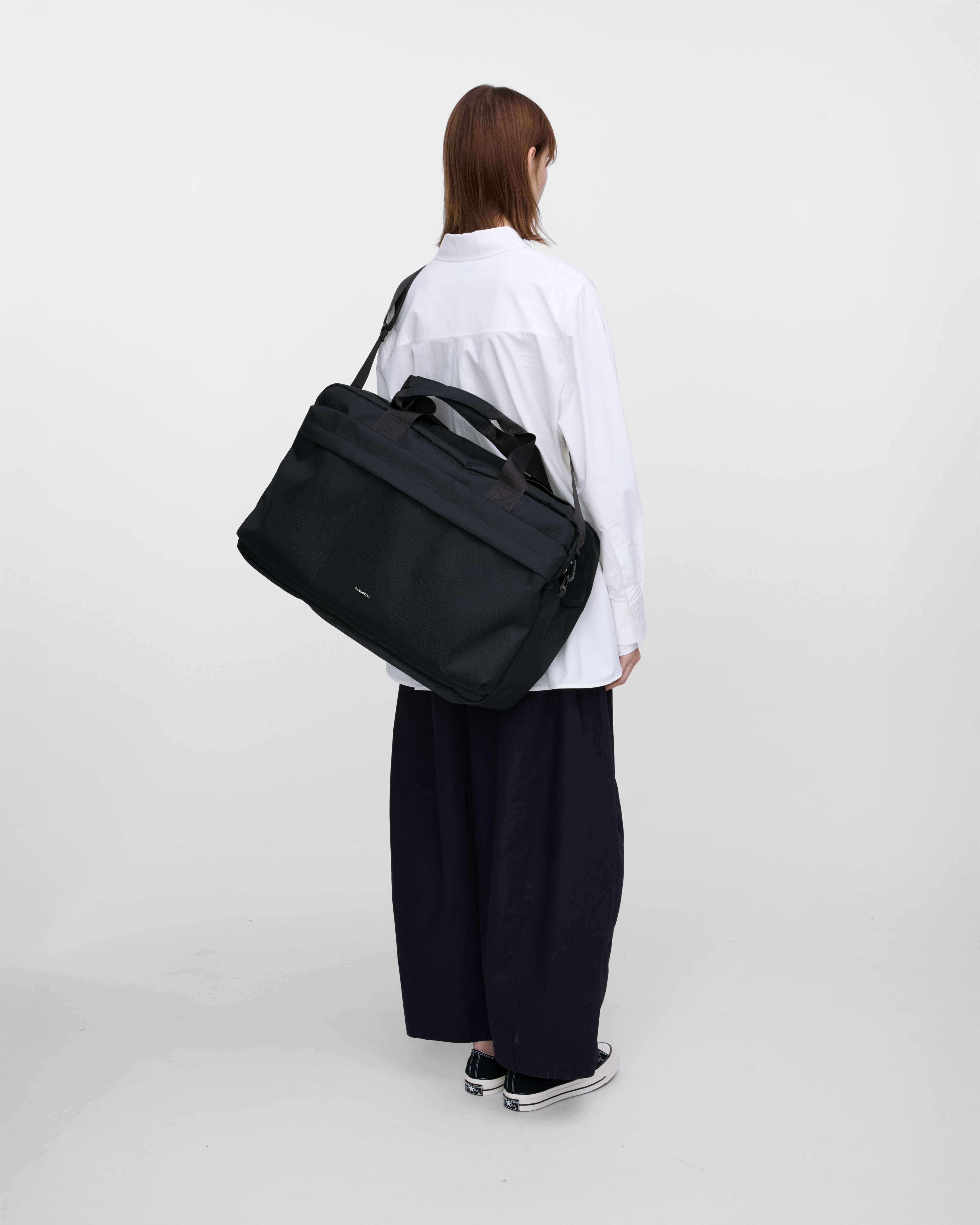 Female model wearing Sandqvist GO Weekender L, black. Back view, wearing the bag on one shoulder crossbody.