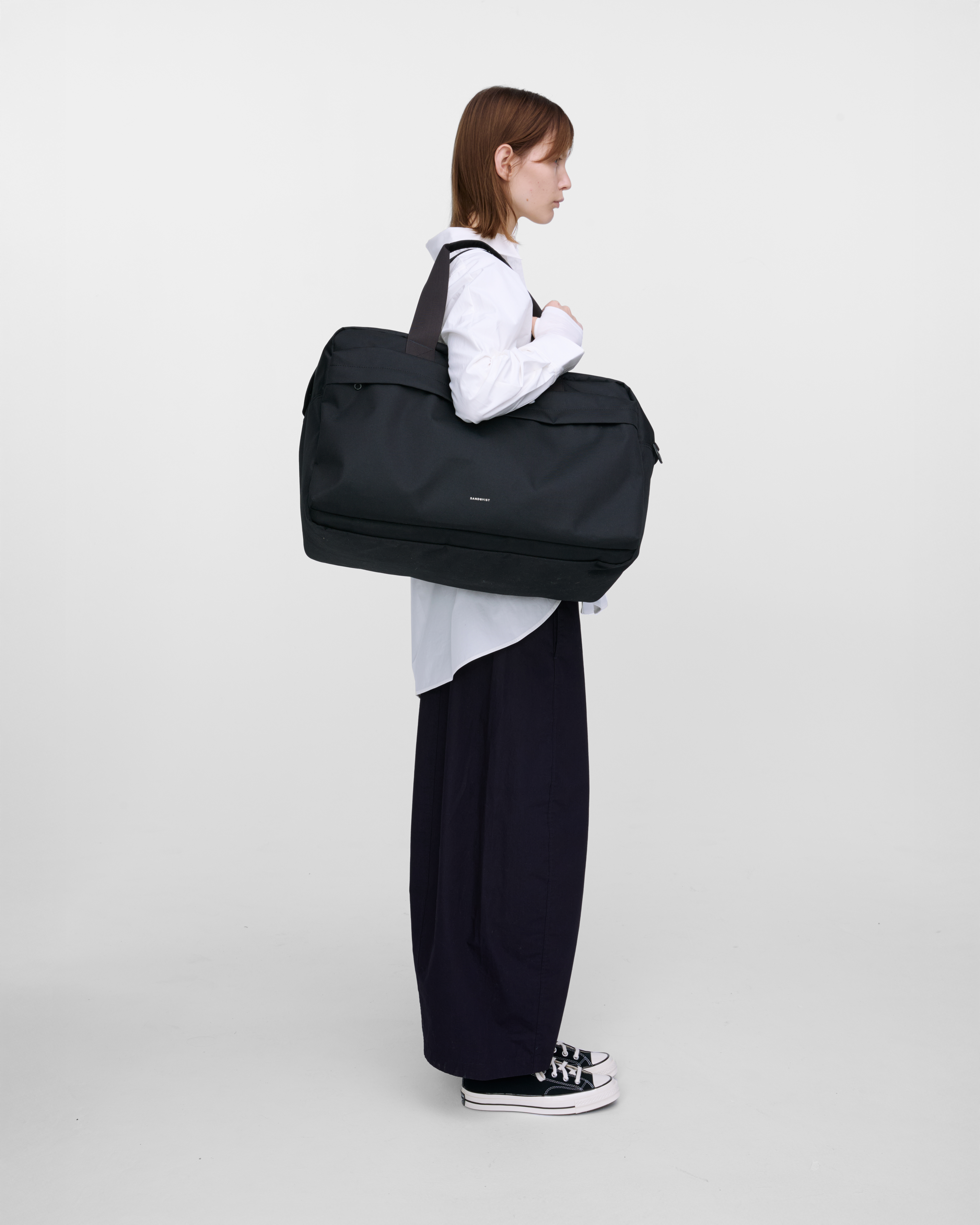 Female model wearing Sandqvist GO Weekender L, black. Side view, wearing the bag on one shoulder. 