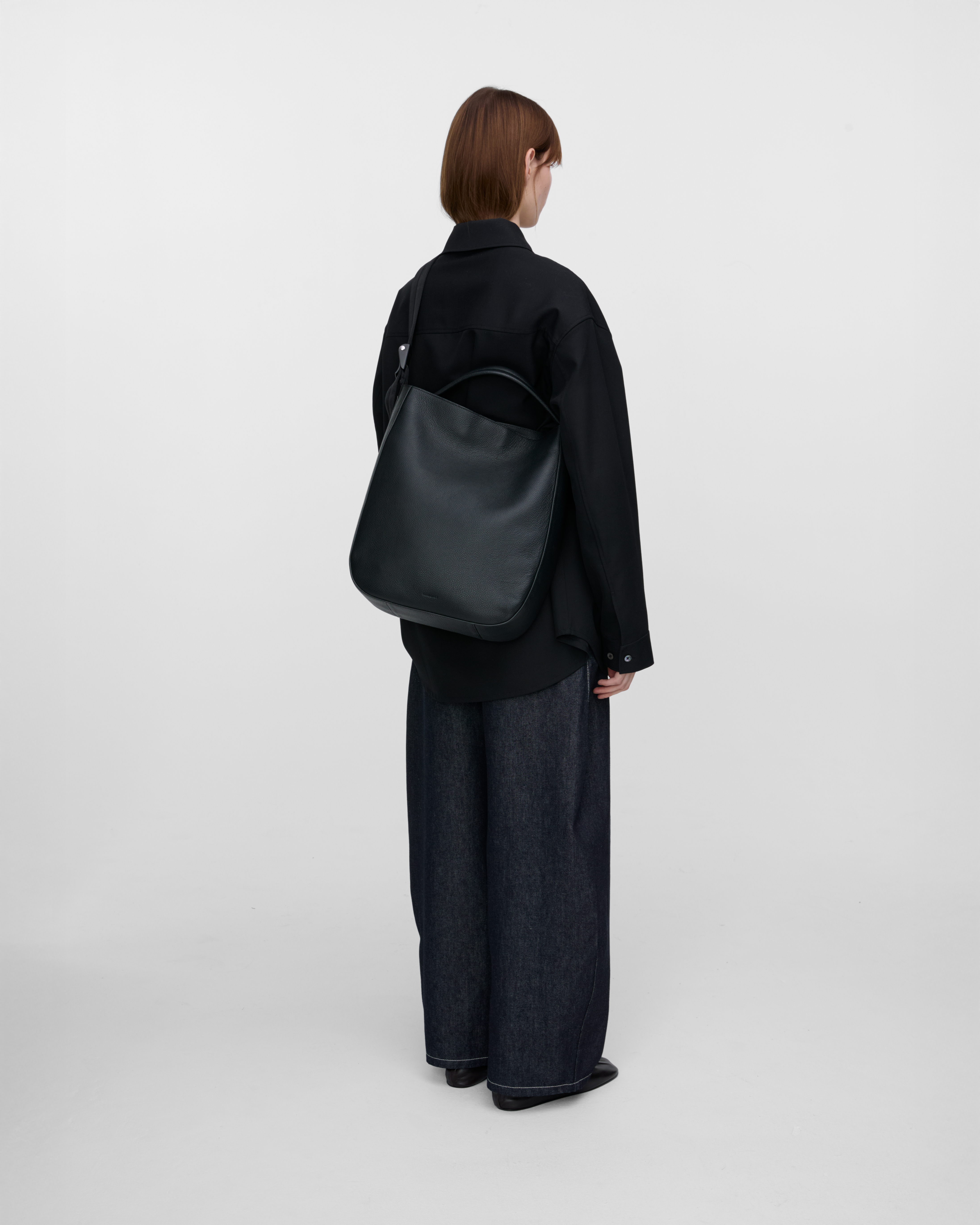 Female model wearing Sandqvist Agile Hobo Tote Bag, black. Back view, wearing the bag on one shoulder crossbody.