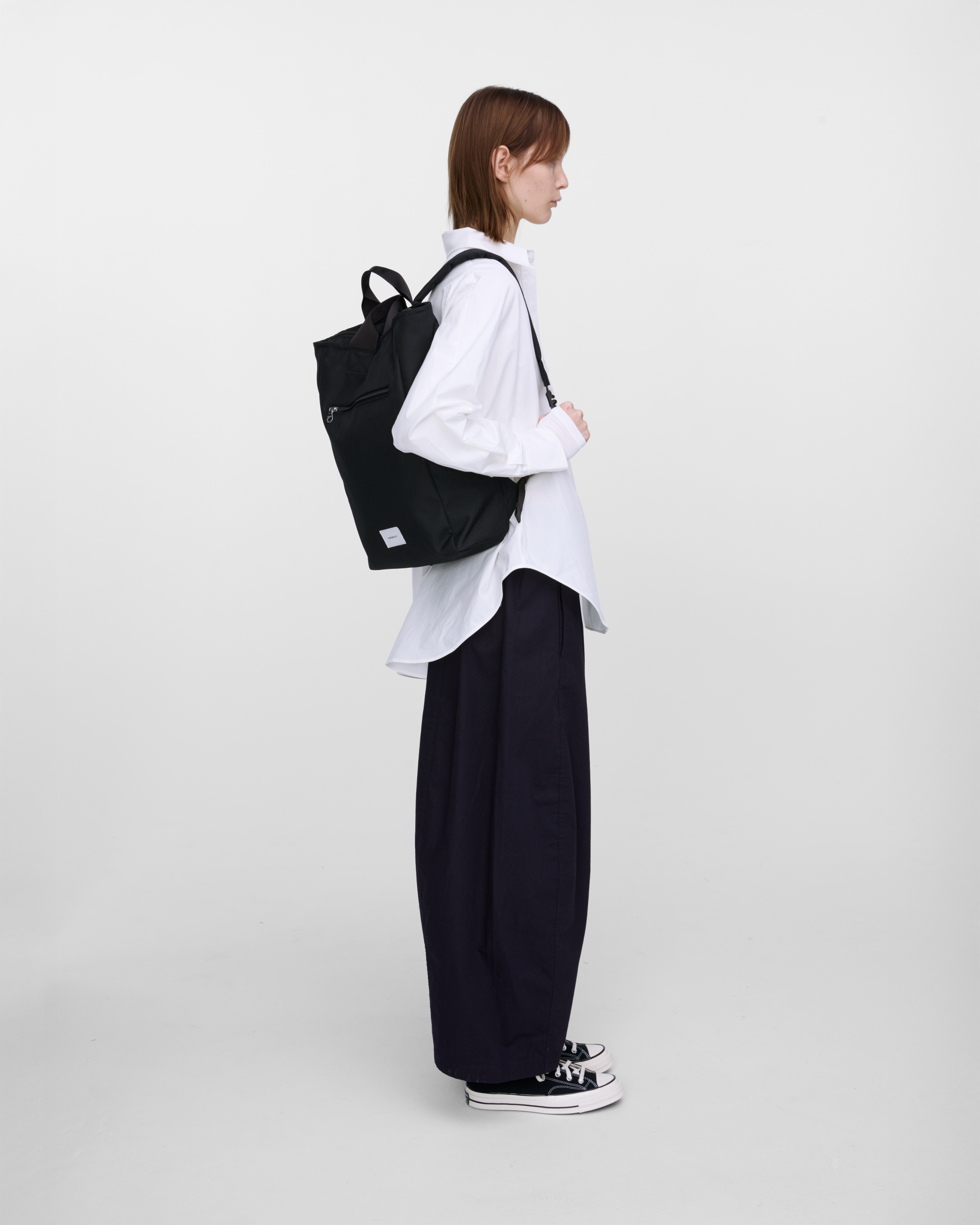 Female model wearing Sandqvist Ground 2-way Bag, black. Side view, wearing the bag on one shoudler.