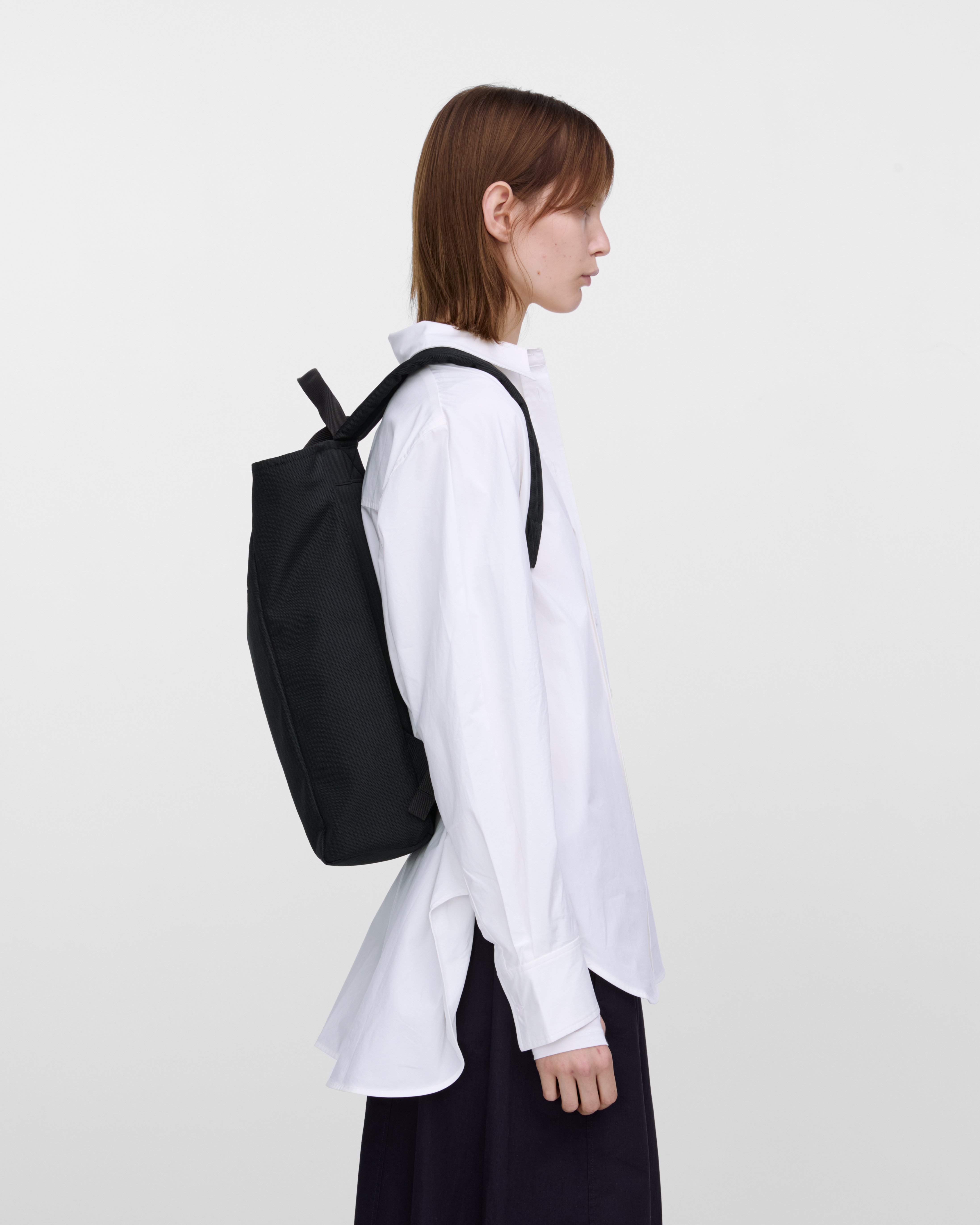 Female model wearing Sandqvist Ground 2-way Bag, black. Side view, wearing the bag on the back.
