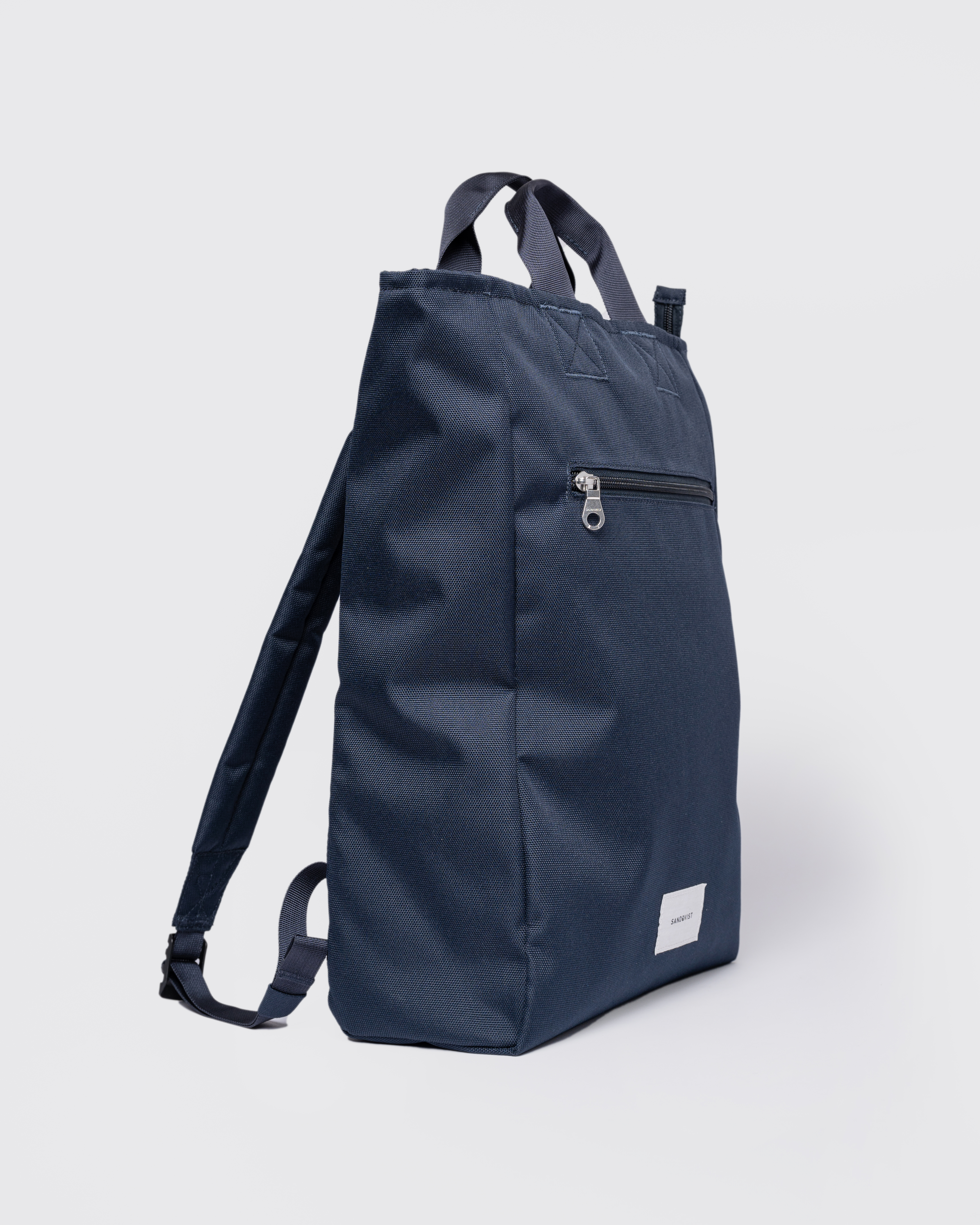 Sandqvist Ground 2-way Bag, blue. Side view, two handles, shoulder straps and a front pocket with a zipper.