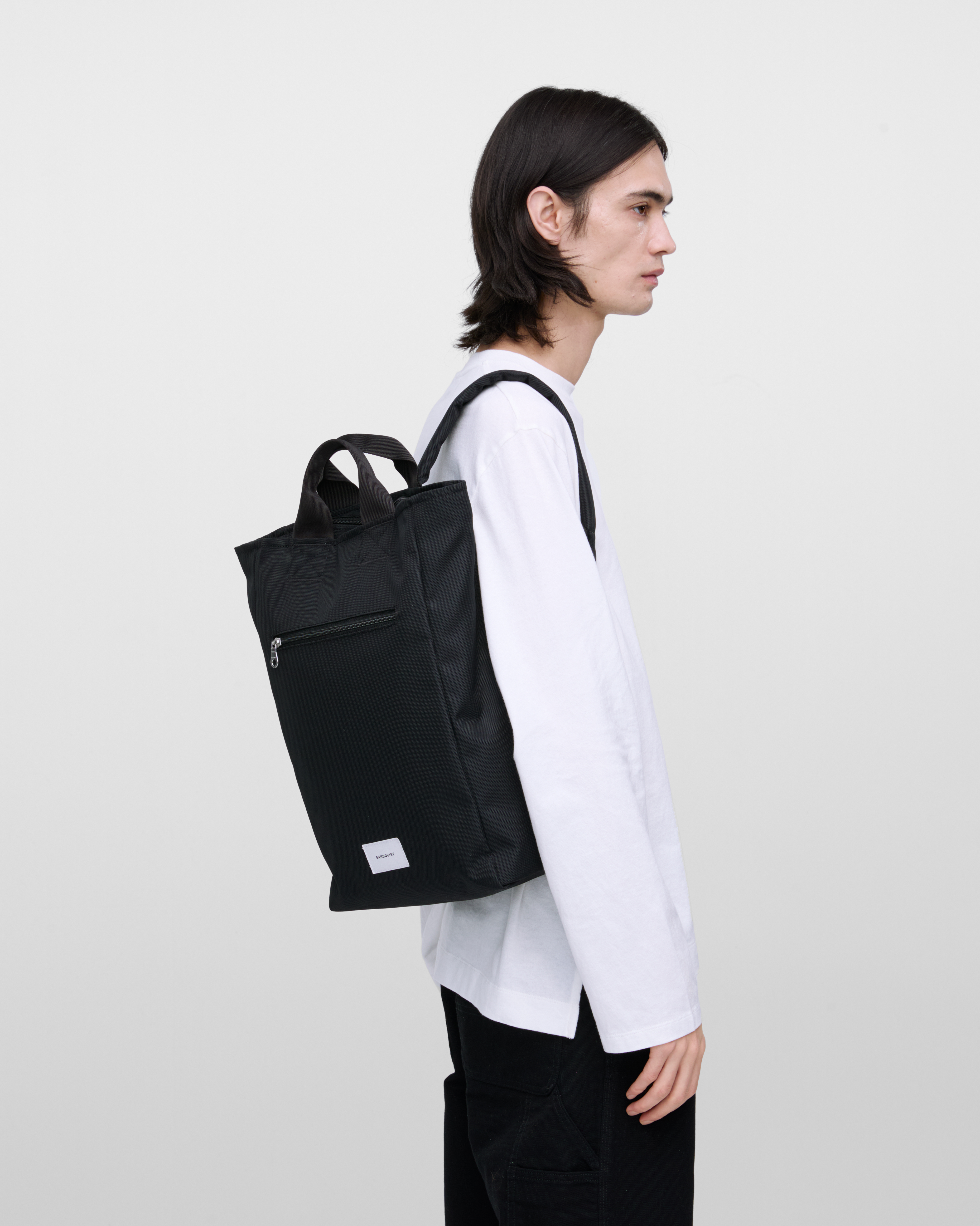Male model wearing Sandqvist Ground 2-way Bag, black. Side view, wearing the bag on one shoulder.
