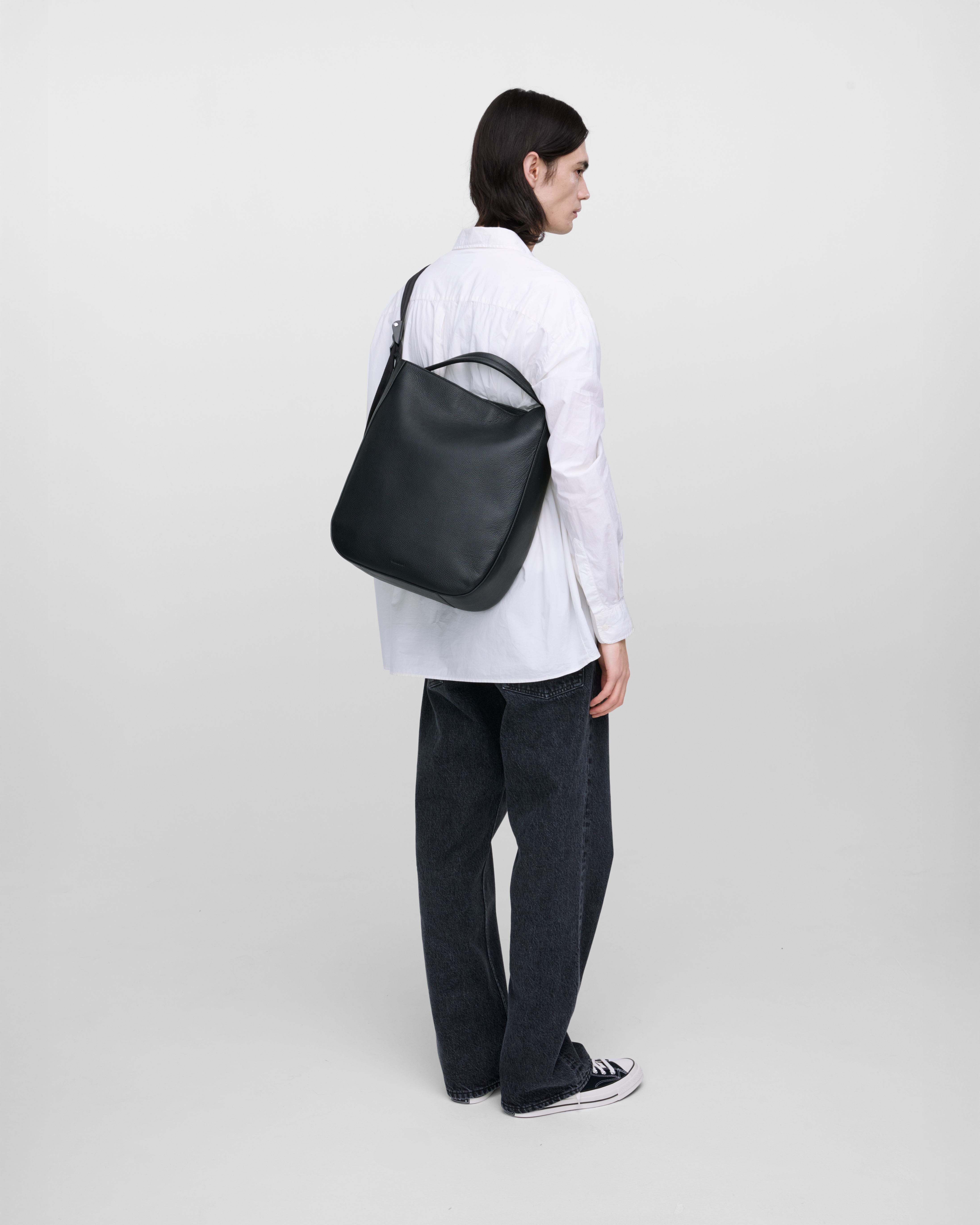 Male model wearing Sandqvist Agile Hobo Tote Bag, black. Back view, wearing the bag on one shoulder crossbody.