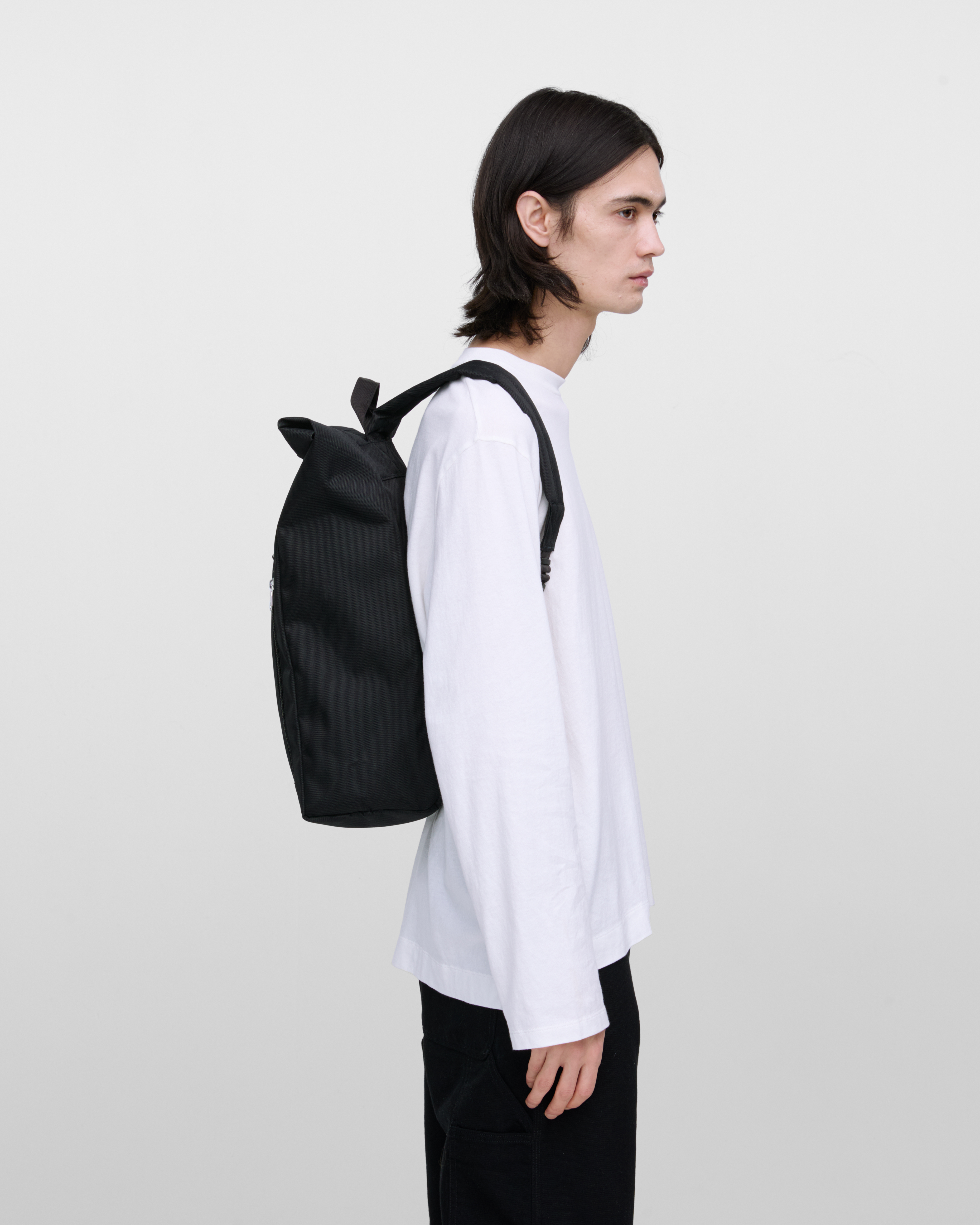 Male model wearing Sandqvist Ground Rolltop Backpack L, black. Side view, wearing the bag on the back.