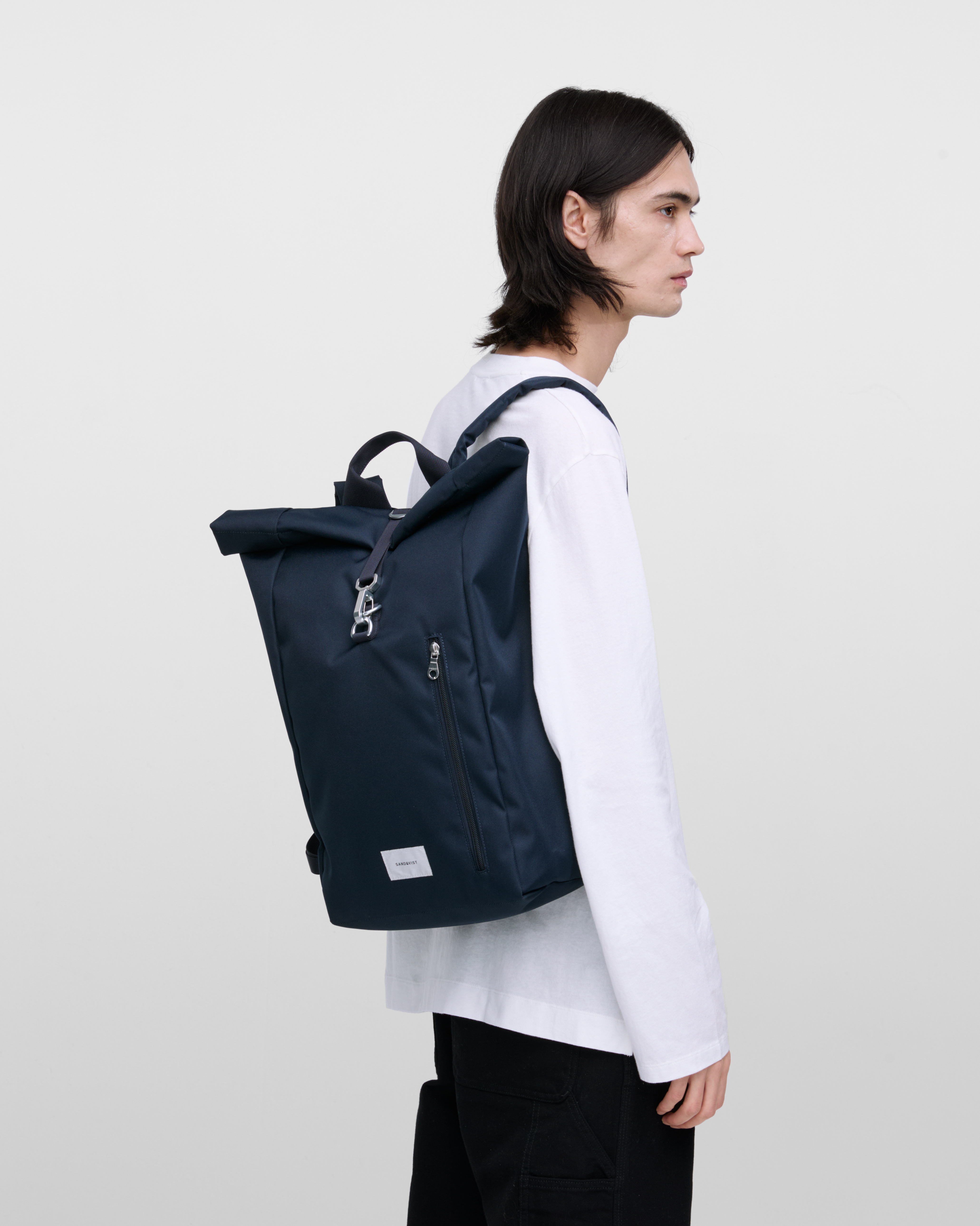 Male model wearing Sandqvist Ground Rolltop Backpack L, blue. Side view, wearing the bag on one shoulder.