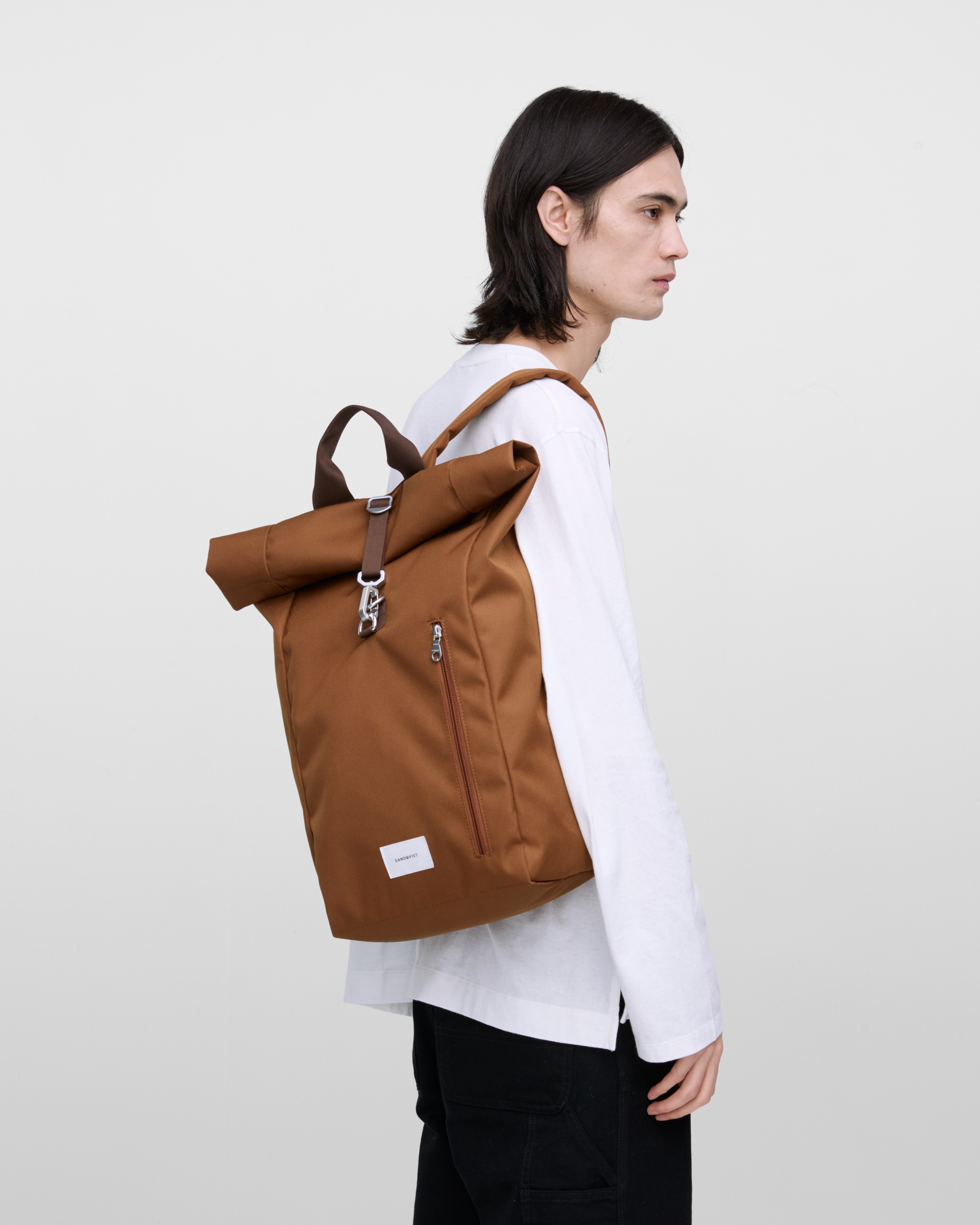 Male model wearing Sandqvist Ground Rolltop Backpack L, brown. Side view, wearing the bag on one shoulder.