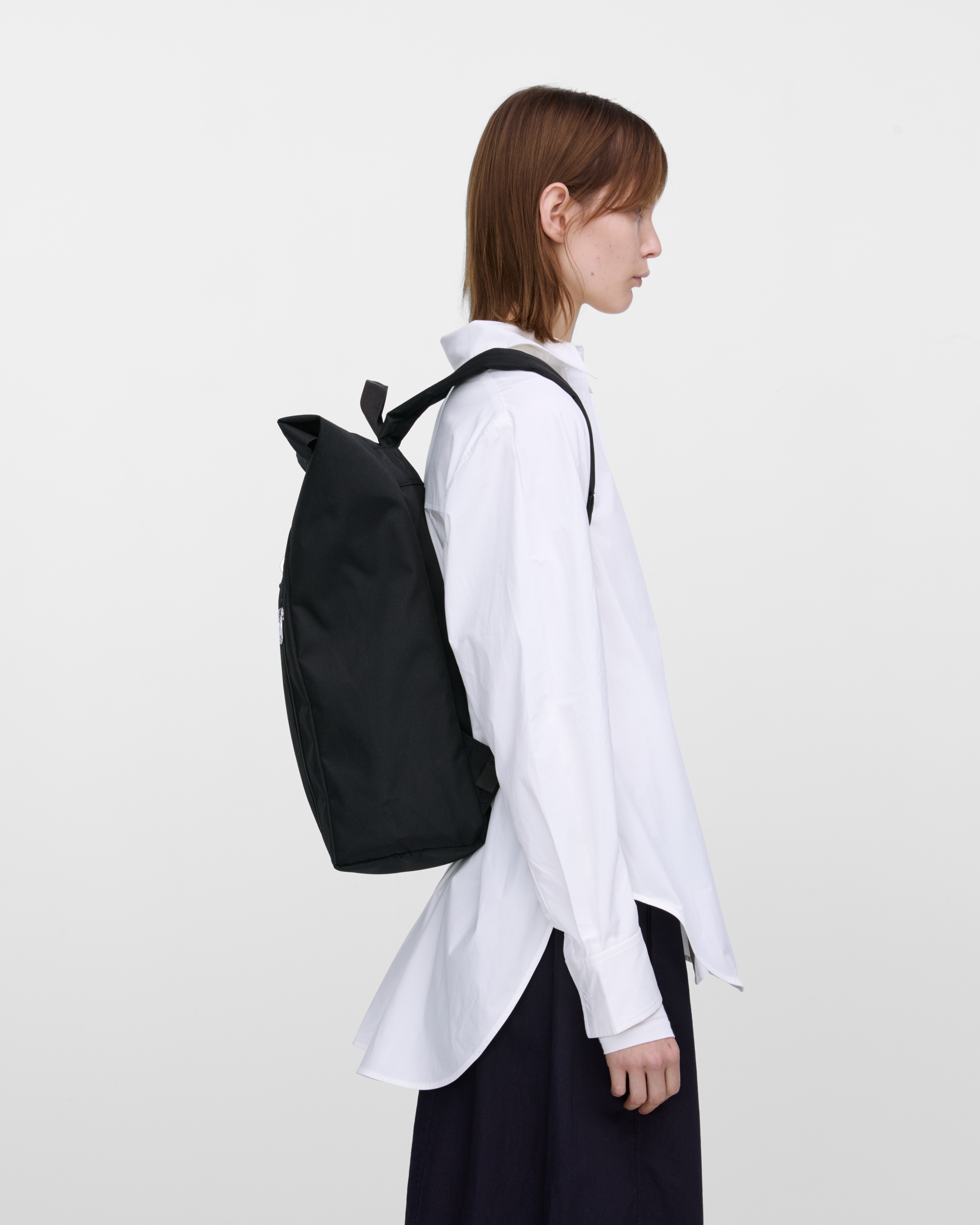 Female model wearing Sandqvist Ground Rolltop Backpack L, black. Side view, wearing the bag on the back.