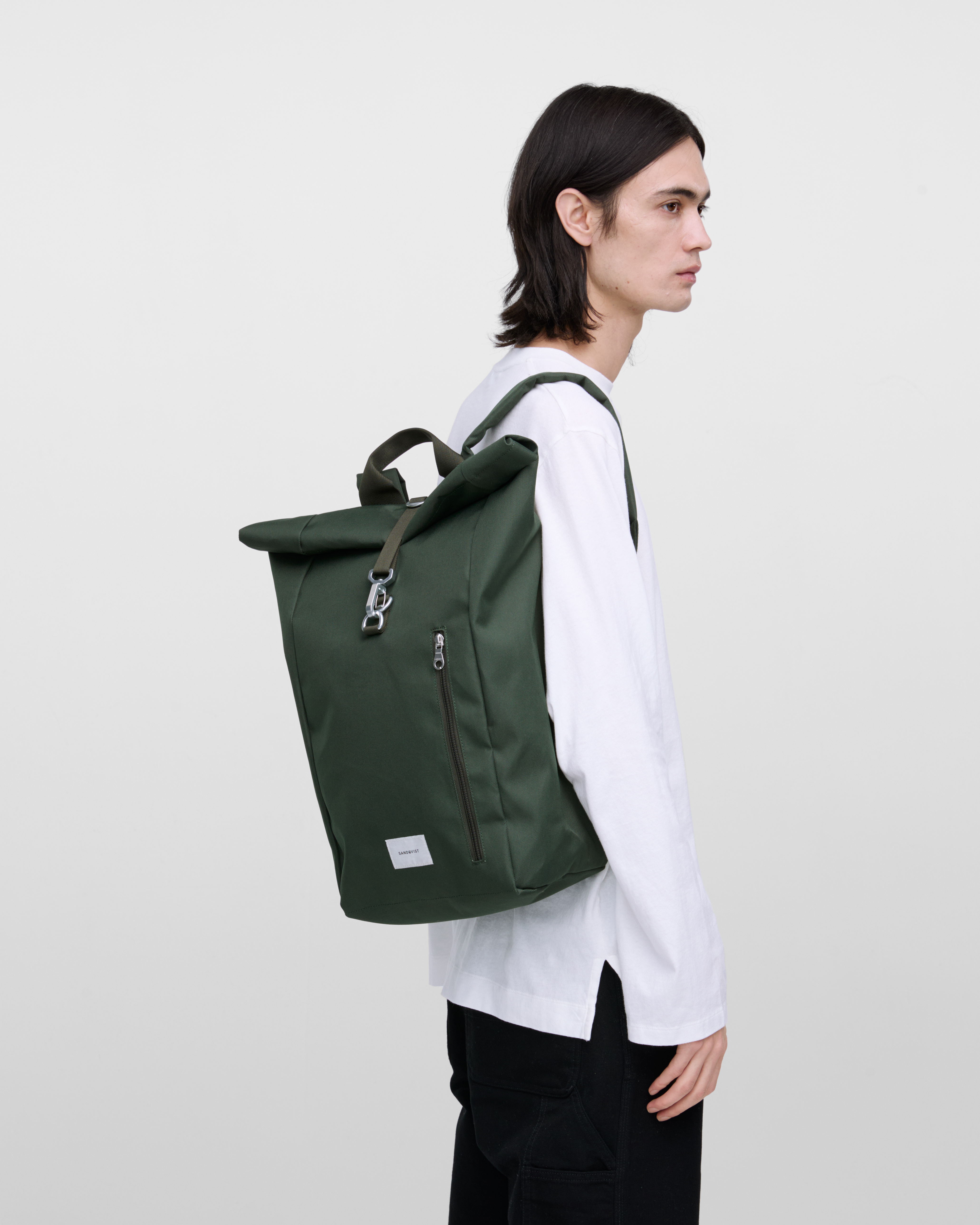 Male model wearing Sandqvist Ground Rolltop Backpack L, green. Side view, wearing the bag on one shoulder.