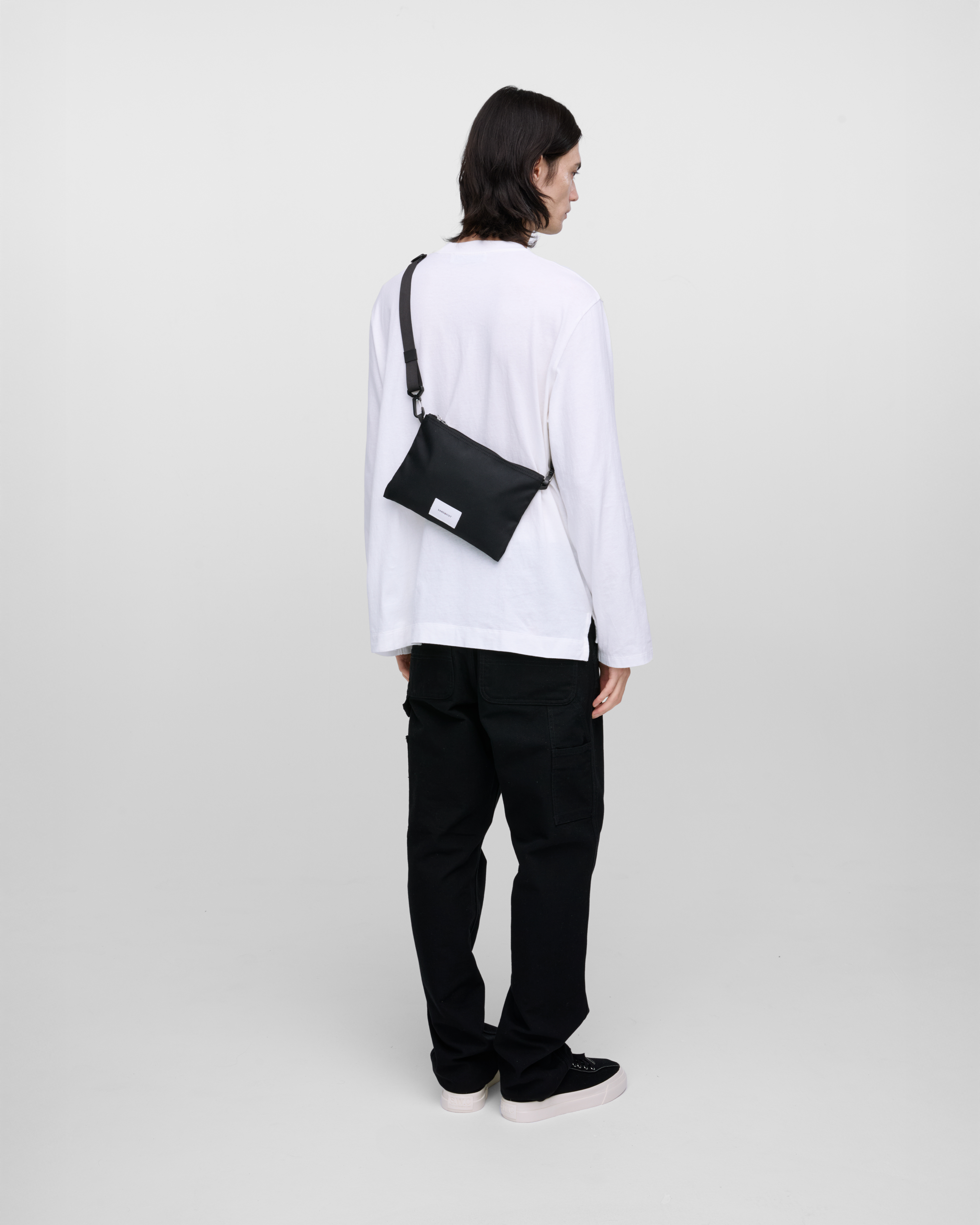 Male model wearing Sandqvist Ground Sacoche Slim, black. Back view, wearing the bag on one shoulder crossbody.