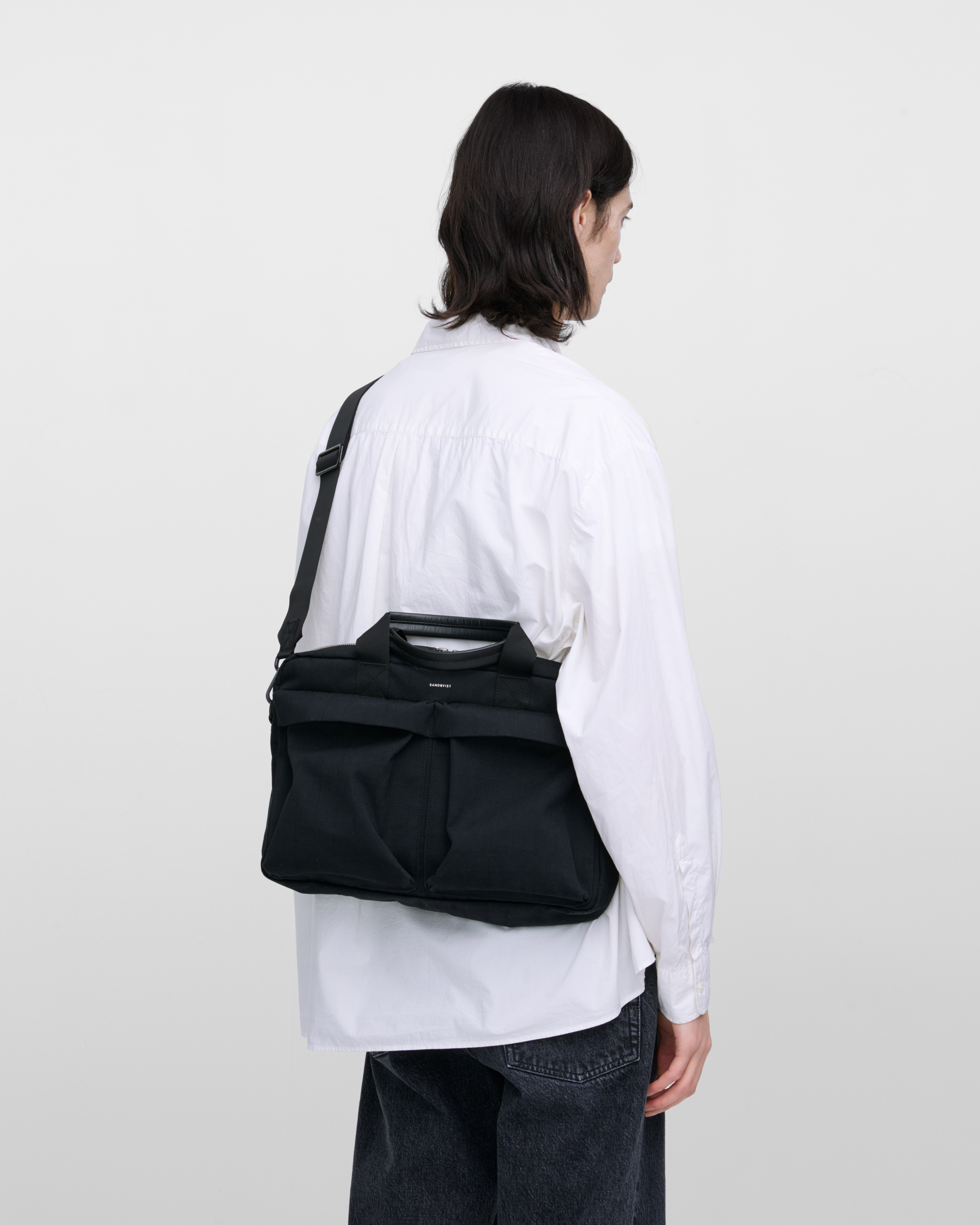 Male model wearing Sandqvist Everyday Briefcase, black. Back view, wearing the bag on one shoulder crossbody, with the bag in the back.