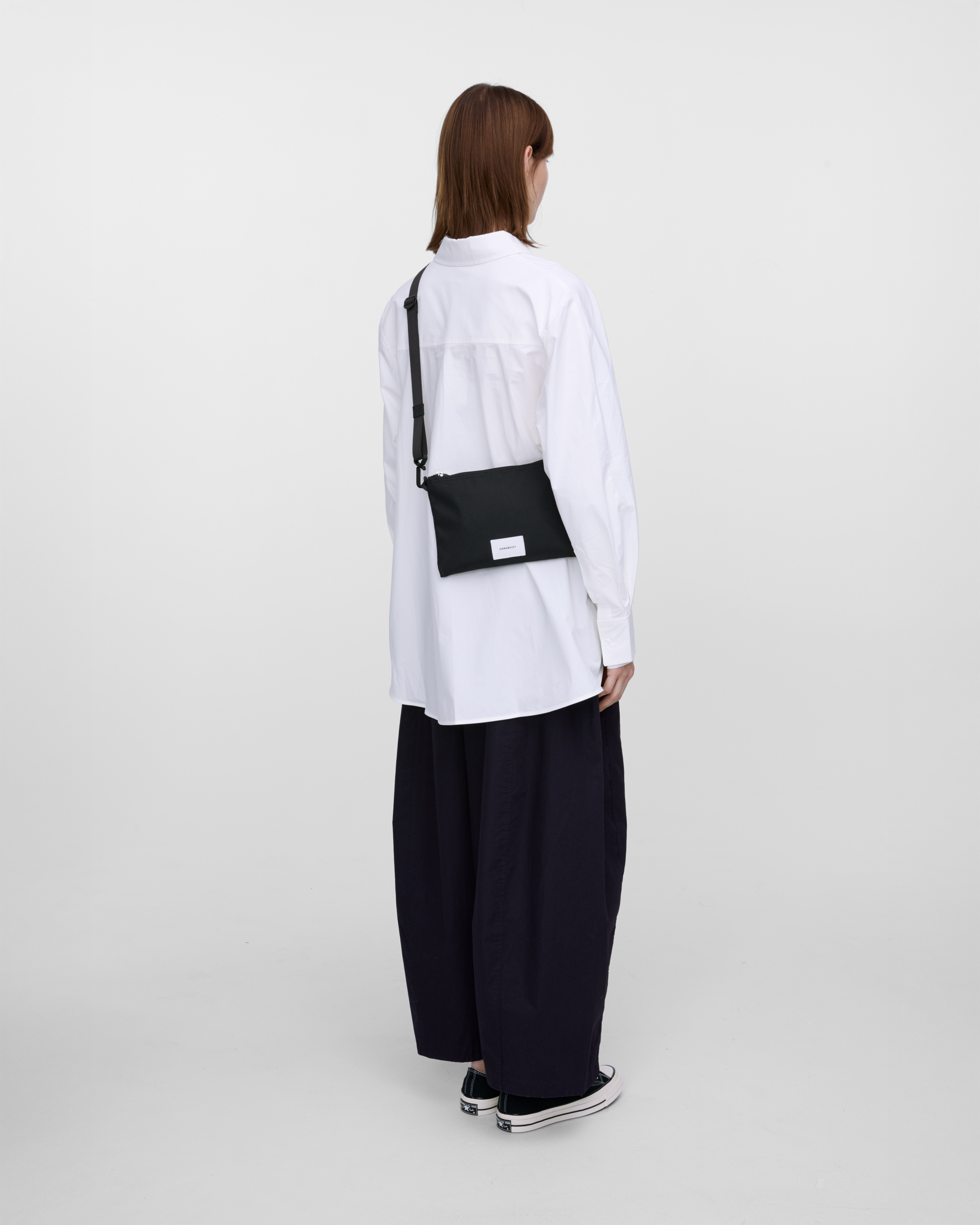 Female model wearing Sandqvist Ground Sacoche Slim, black. Back view, wearing the bag on one shoulder crossbody.