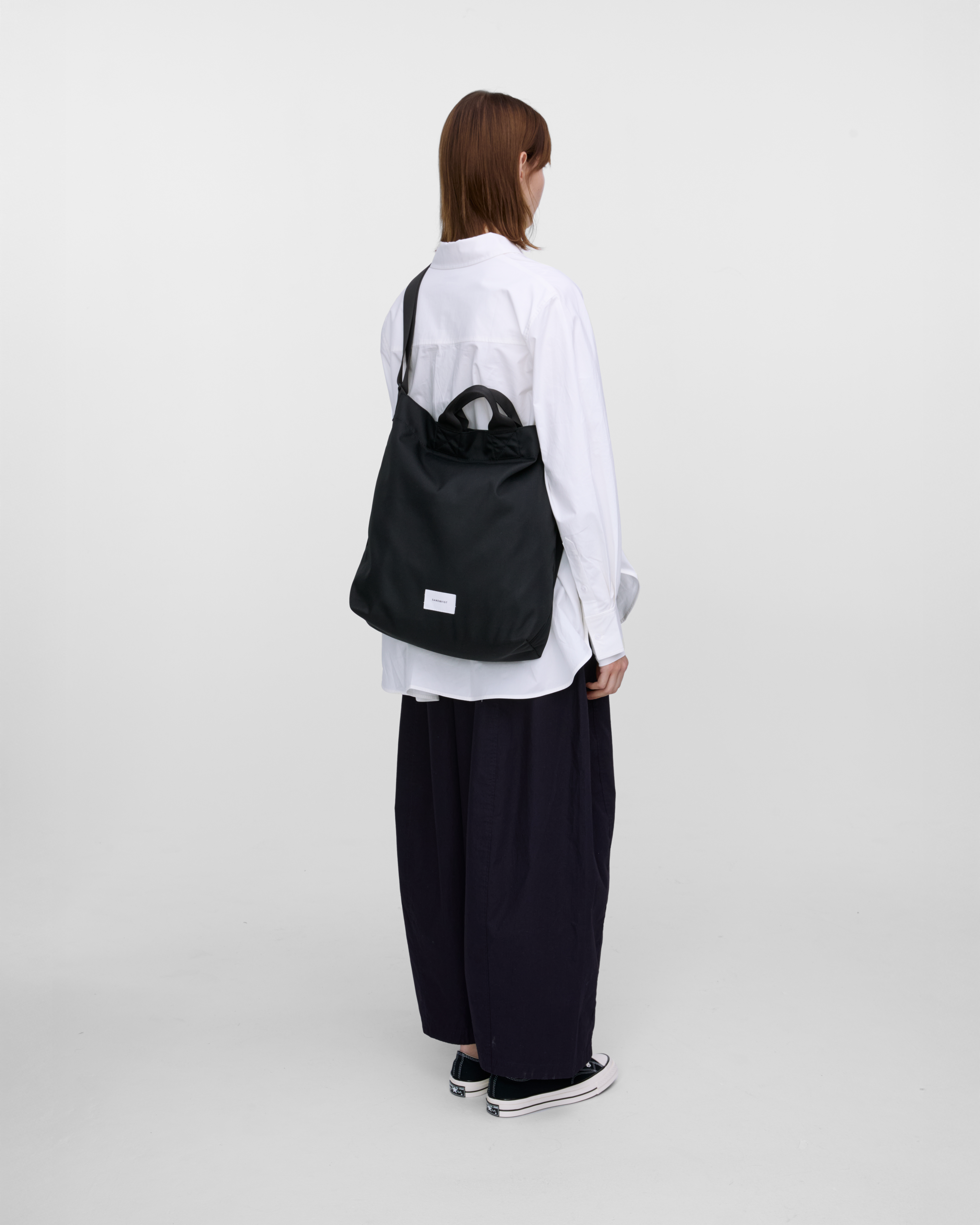 Female model wearing Sandqvist Ground Shopper Bag, black. Back view, wearing the bag on one shoulder crossbody.