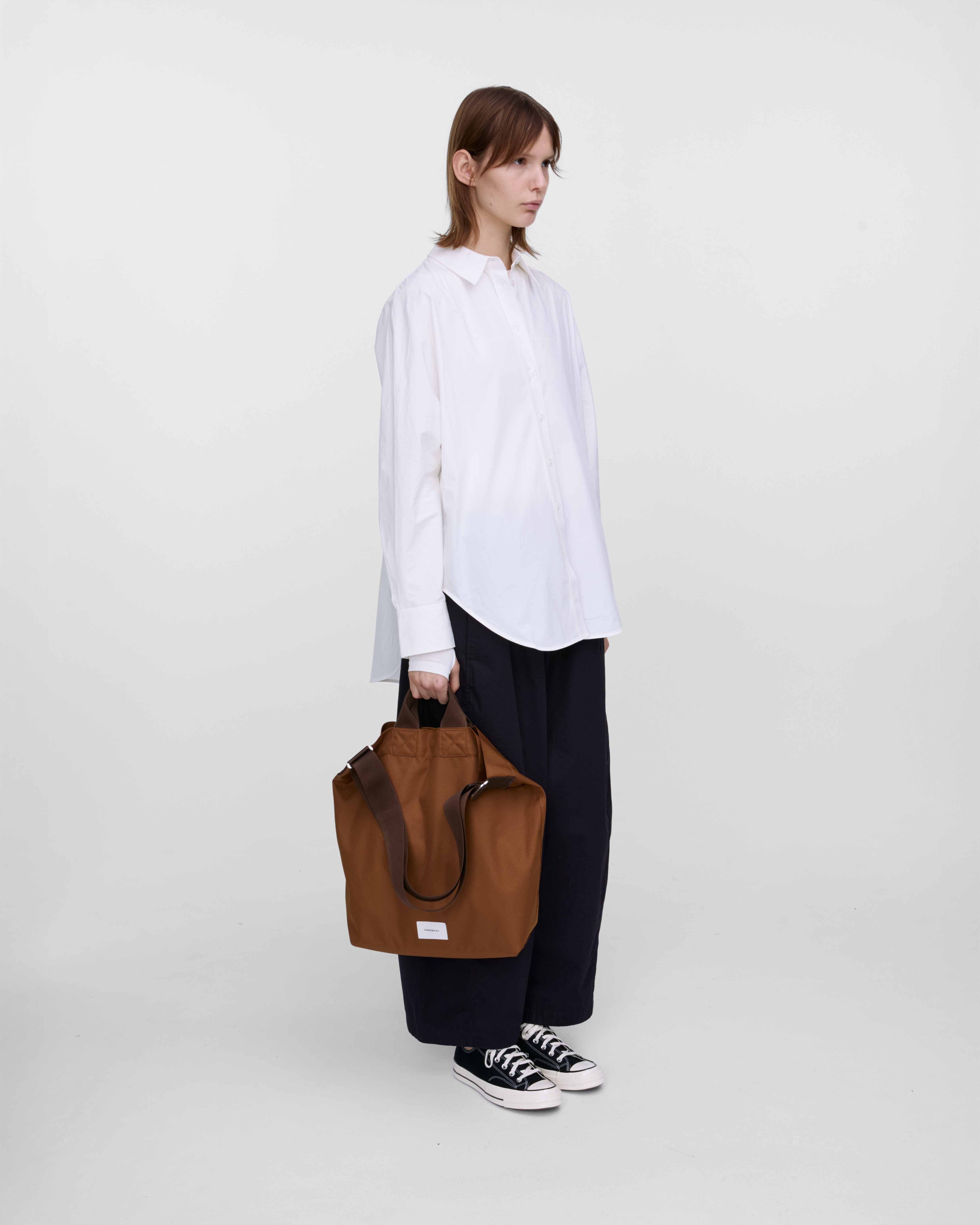 Mannequin féminin tenant un sac Sandqvist Ground Shopper, marron. Vue de profil, tenant le sac dans une main.