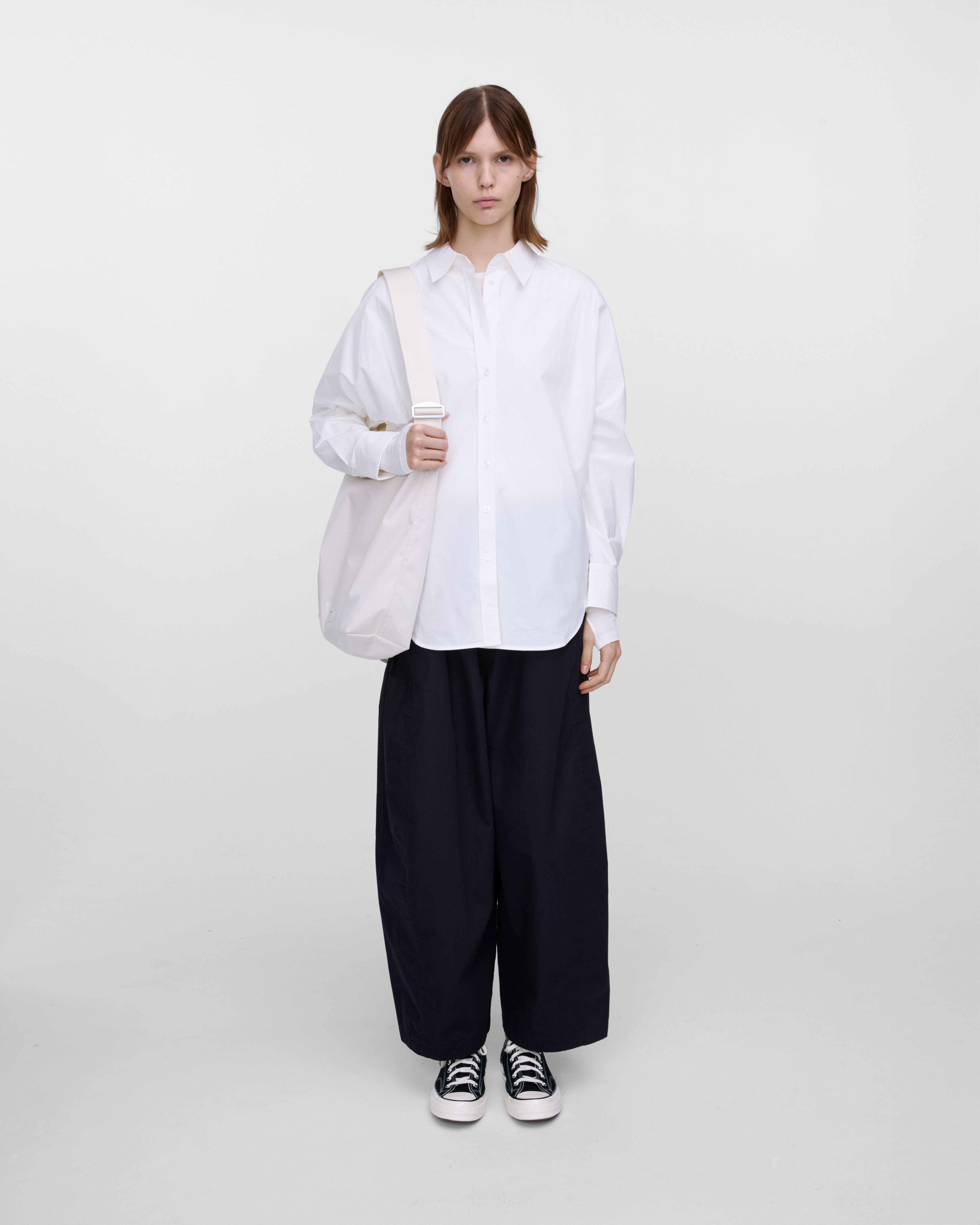 Female model wearing Sandqvist Ground Shopper Bag, white. Front view, wearing the bag on one shoulder.