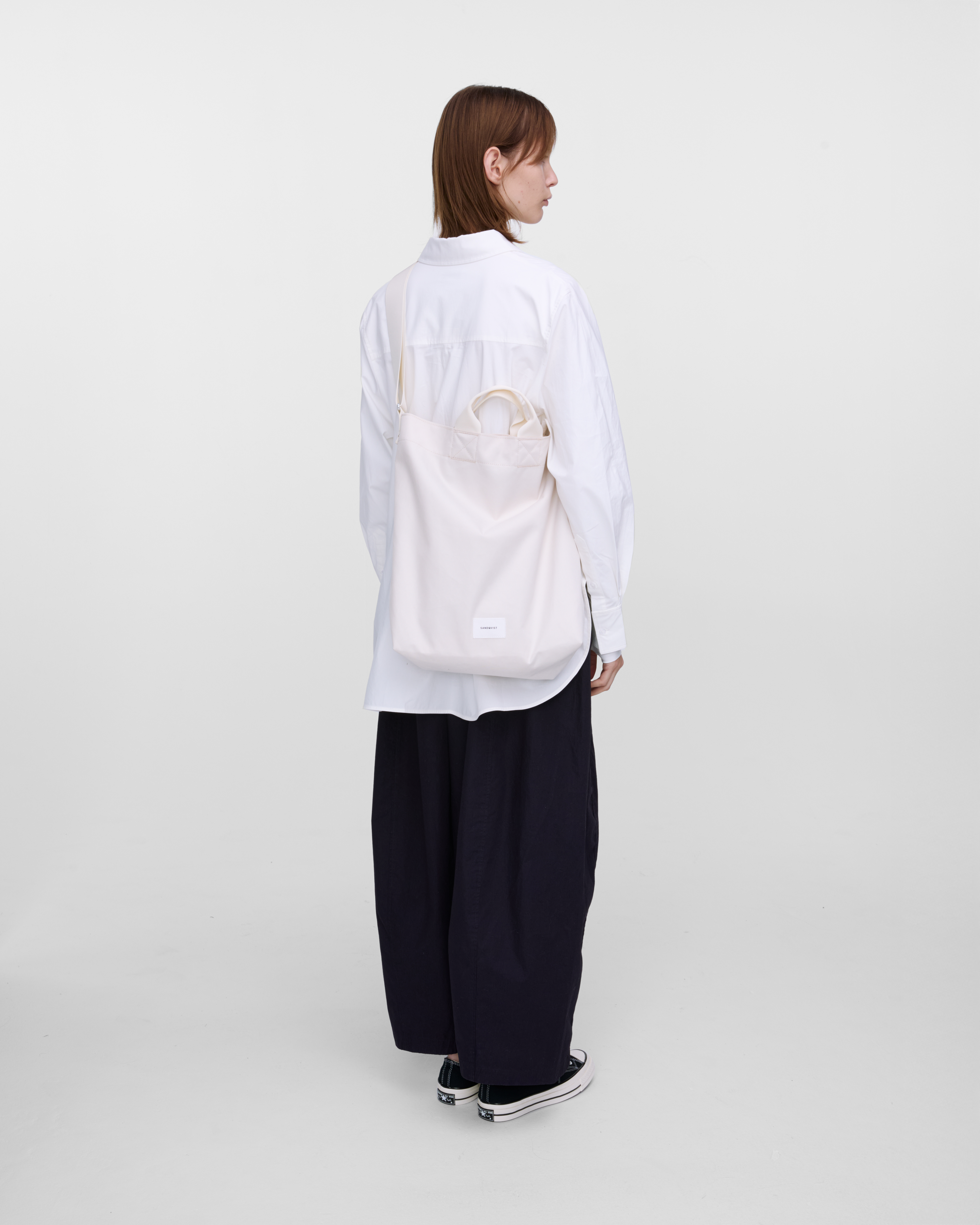 Female model wearing Sandqvist Ground Shopper Bag, white. Back view, wearing the bag on one shoulder crossbody.