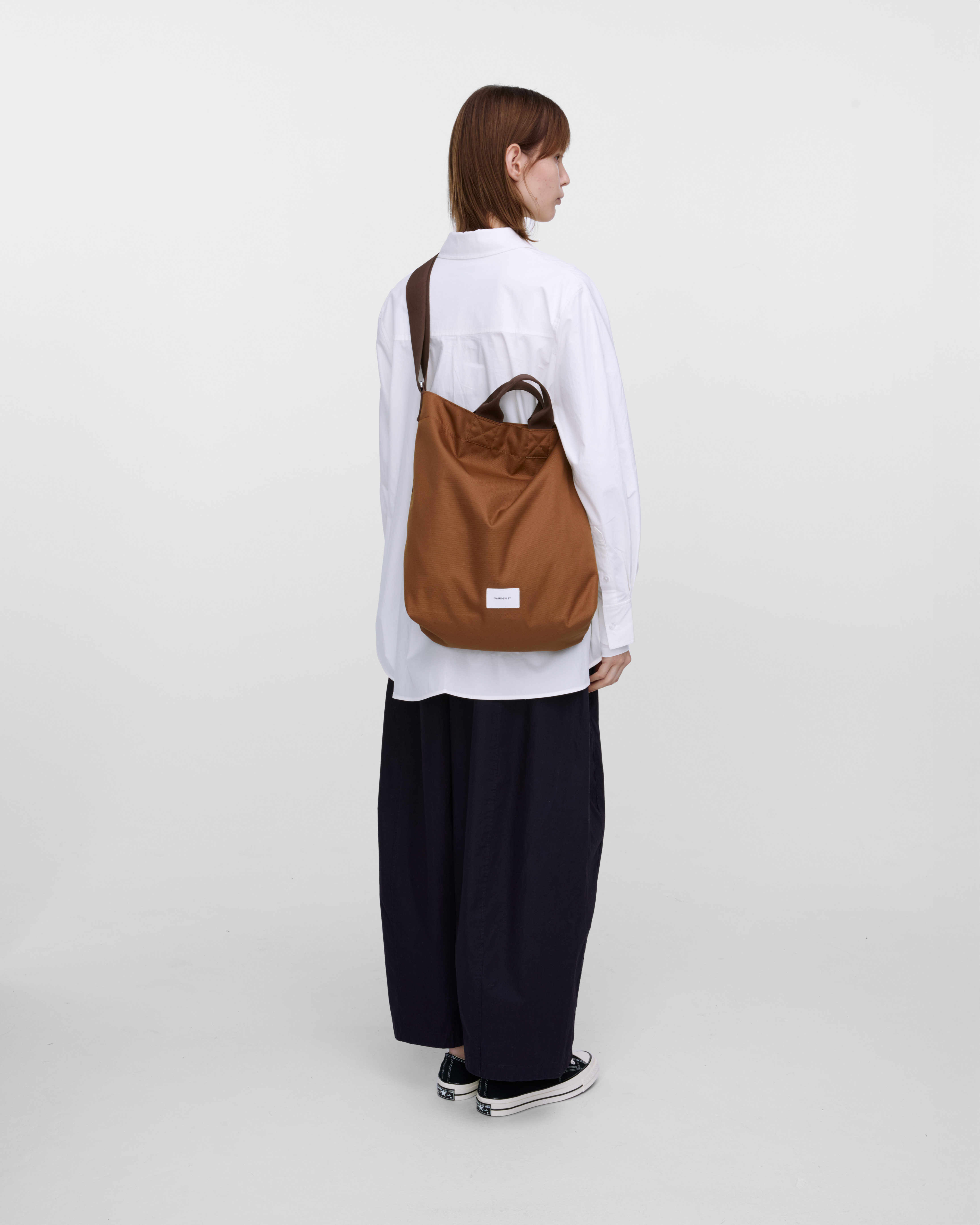 Female model wearing Sandqvist Ground Shopper Bag, brown. Back view, wearing the bag on one shoulder crossbody.