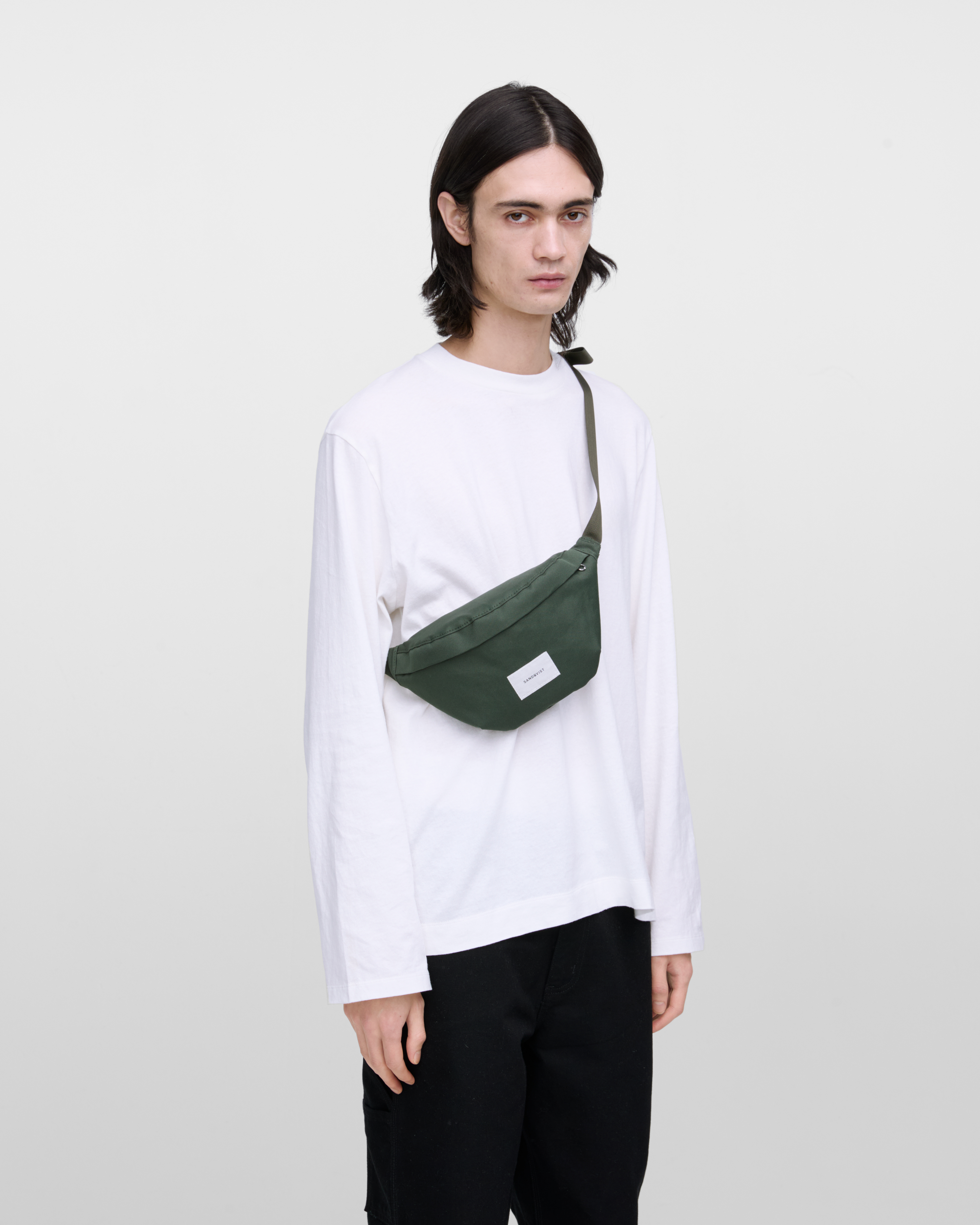 Male model wearing Sandqvist Ground Crossbody Bag, green. Front view, wearing the bag on one shoulder crossbody.