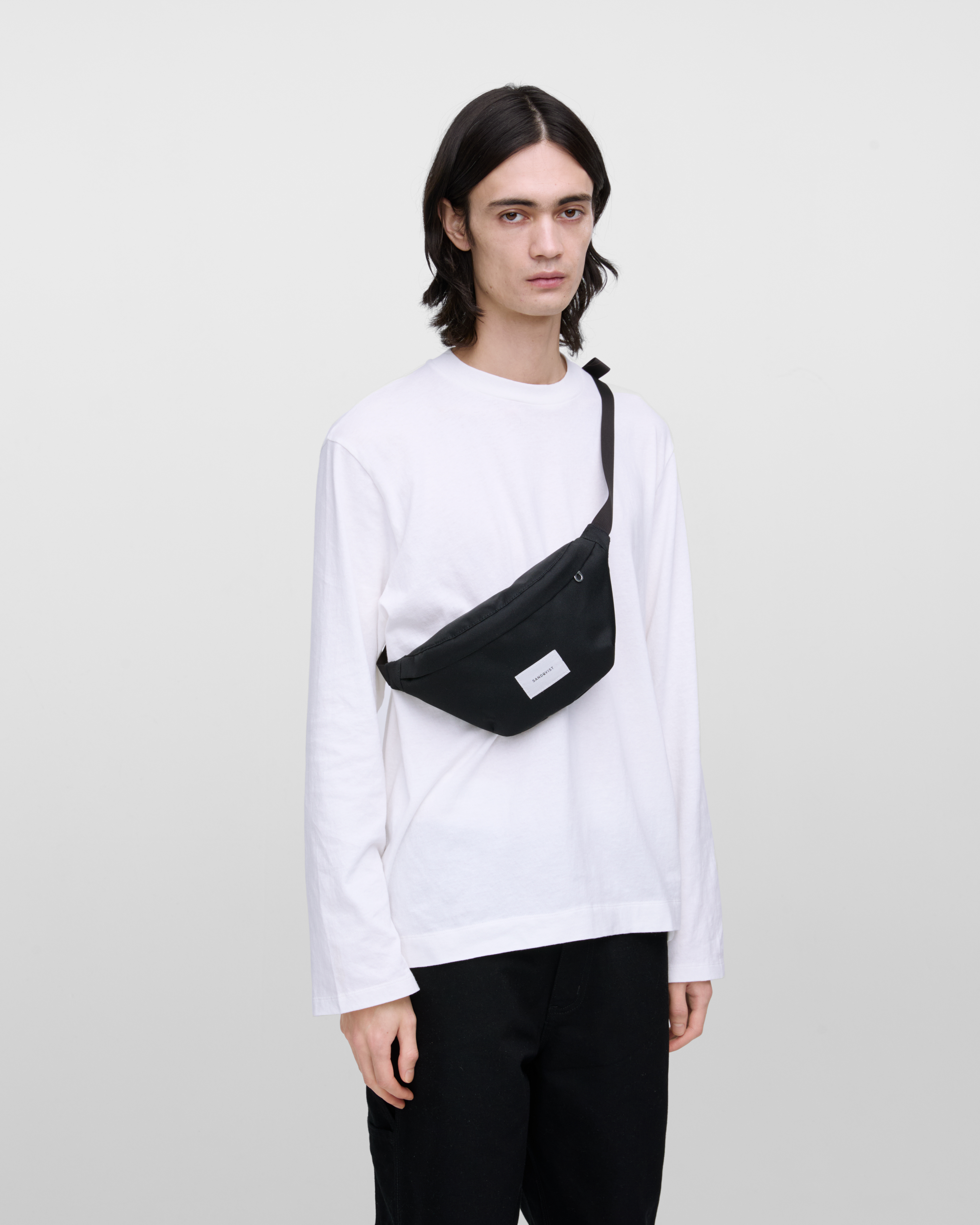 Male model wearing Sandqvist Ground Crossbody Bag, black. Front view, wearing the bag on one shoulder crossbody.