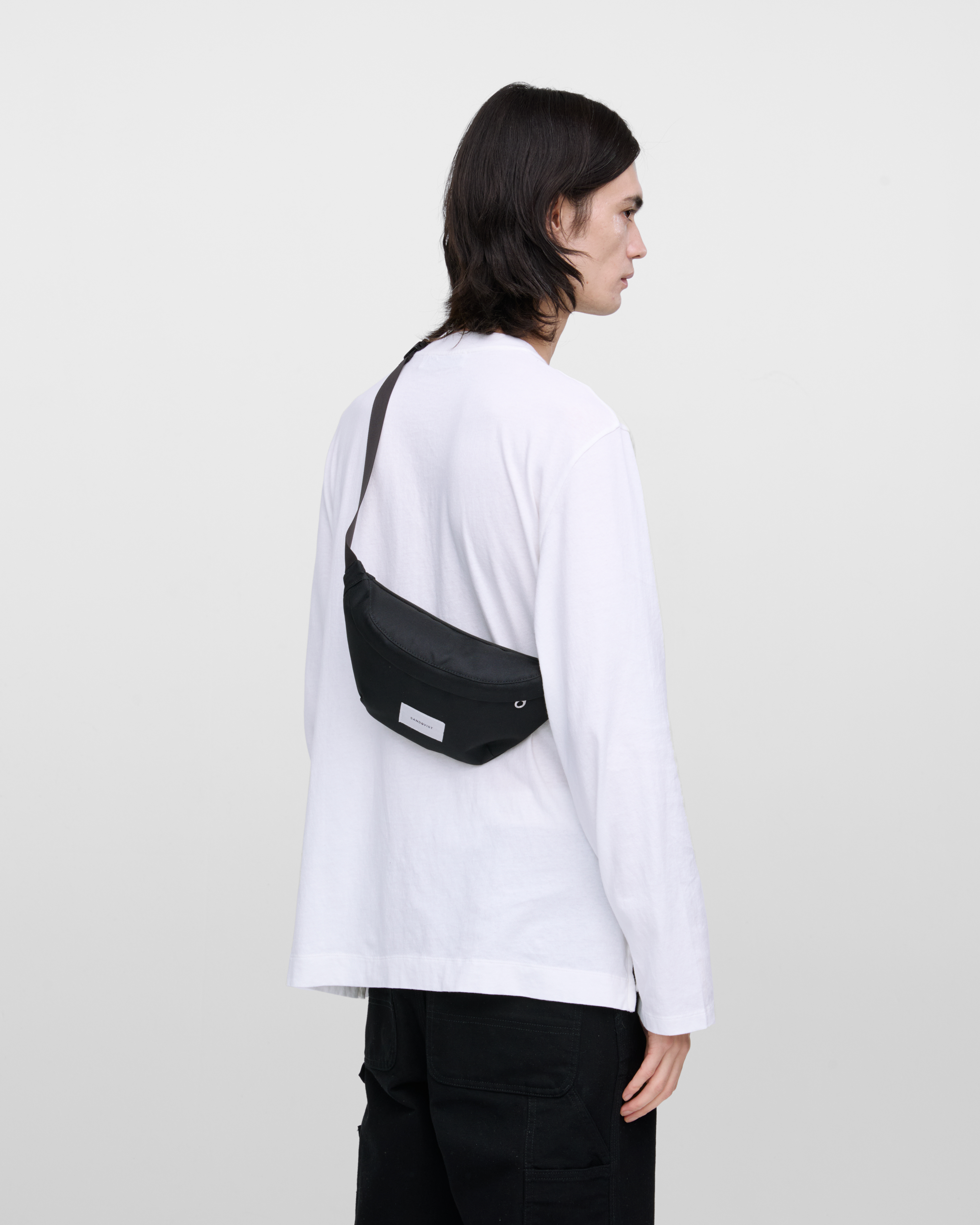 Male model wearing Sandqvist Ground Crossbody Bag, black. Back view, wearing the bag on one shoulder crossbody.