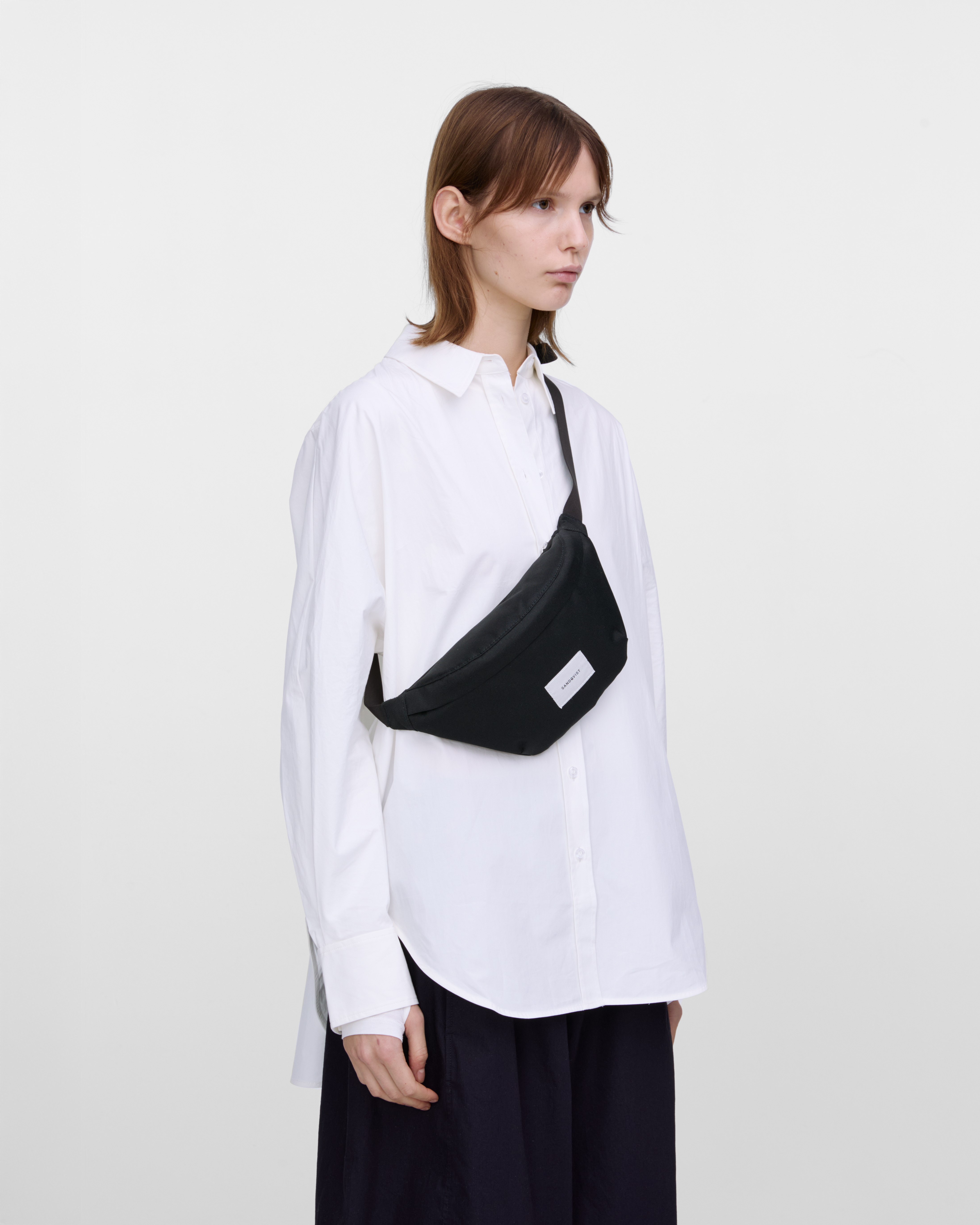 Female model wearing Sandqvist Ground Crossbody Bag, black. Front view, wearing the bag on one shoulder crossbody.