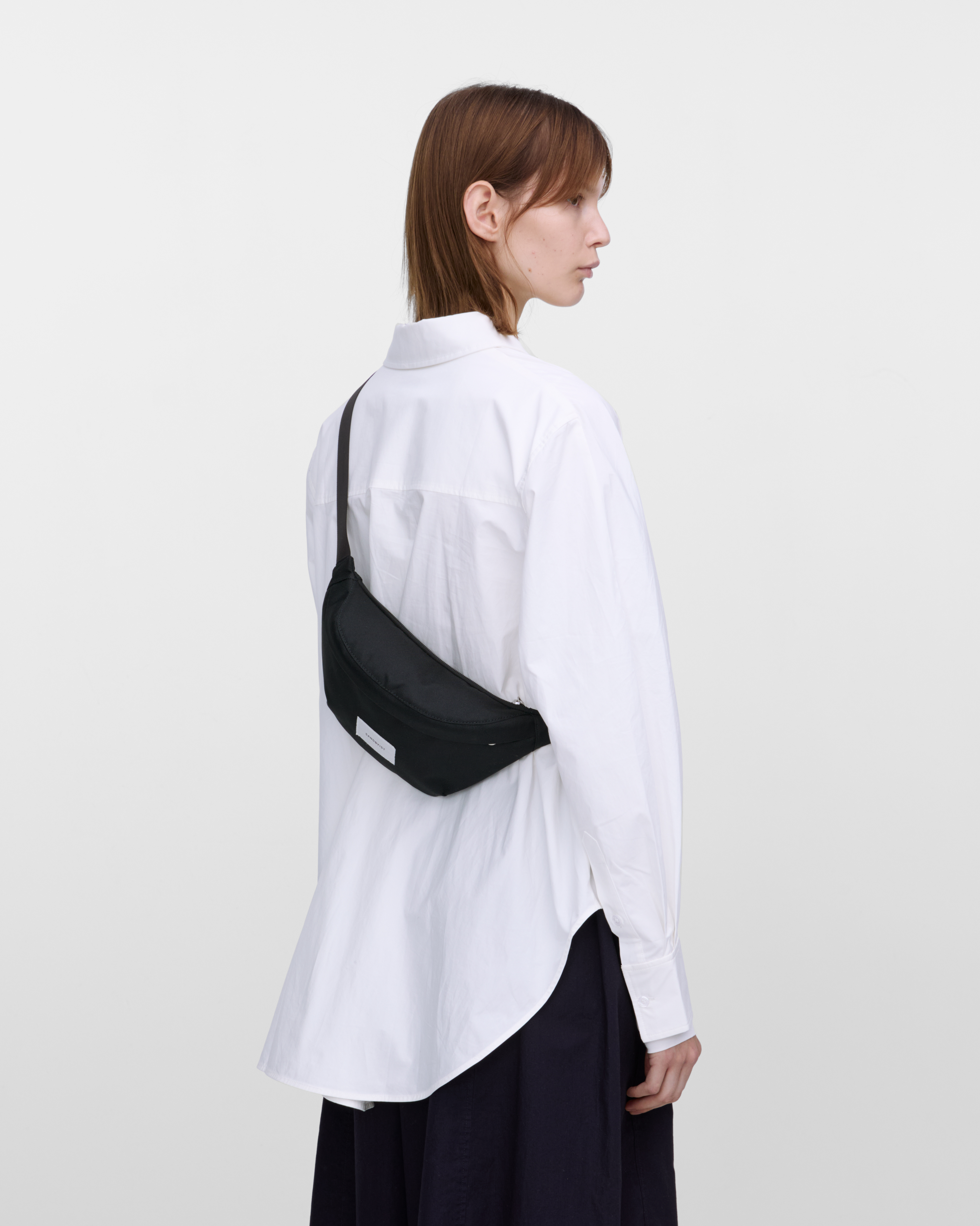 Female model wearing Sandqvist Ground Crossbody Bag, black. Back view, wearing the bag on one shoulder crossbody.