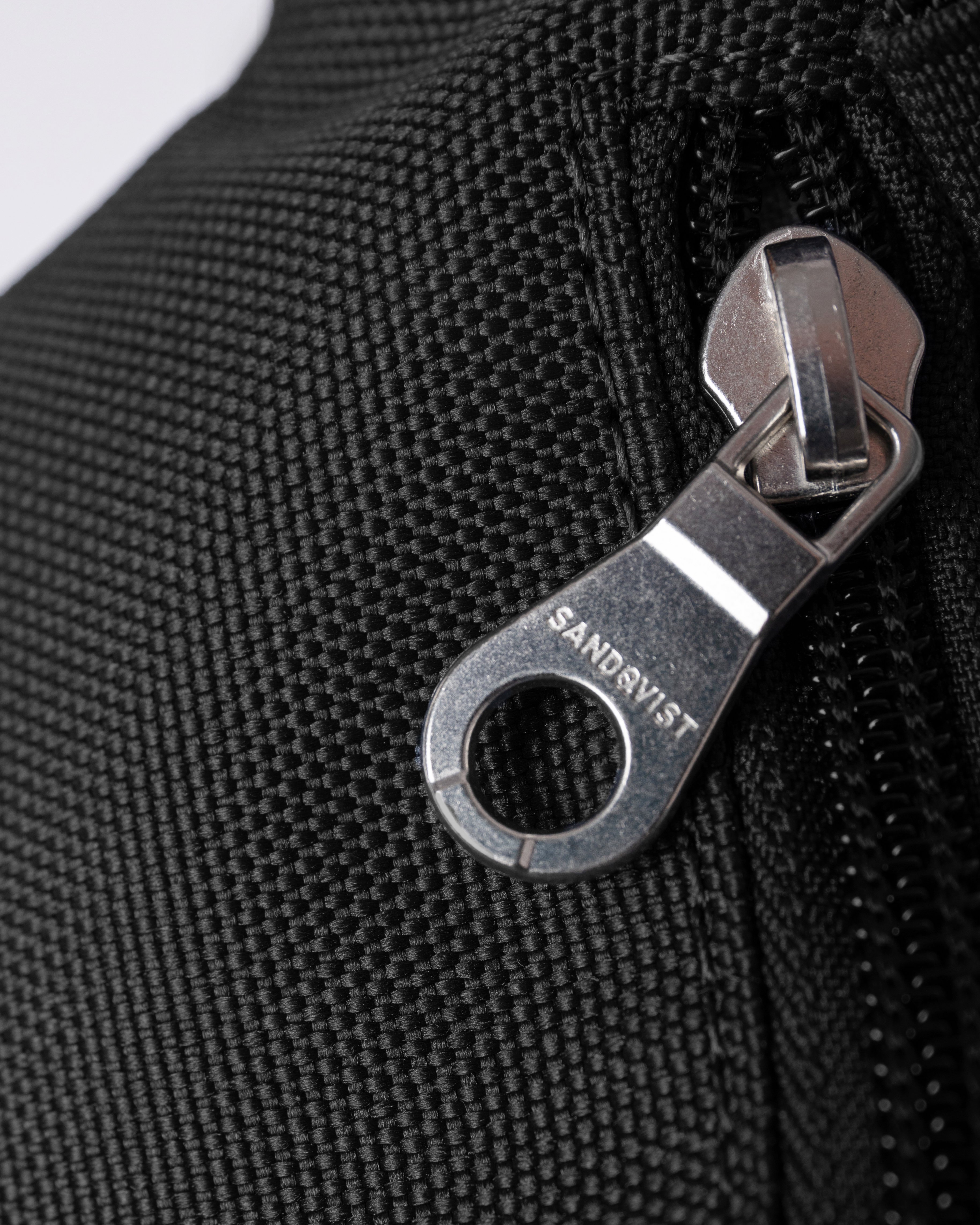 Sandqvist Ground Crossbody Bag, black. Close-up of zipper-puller.