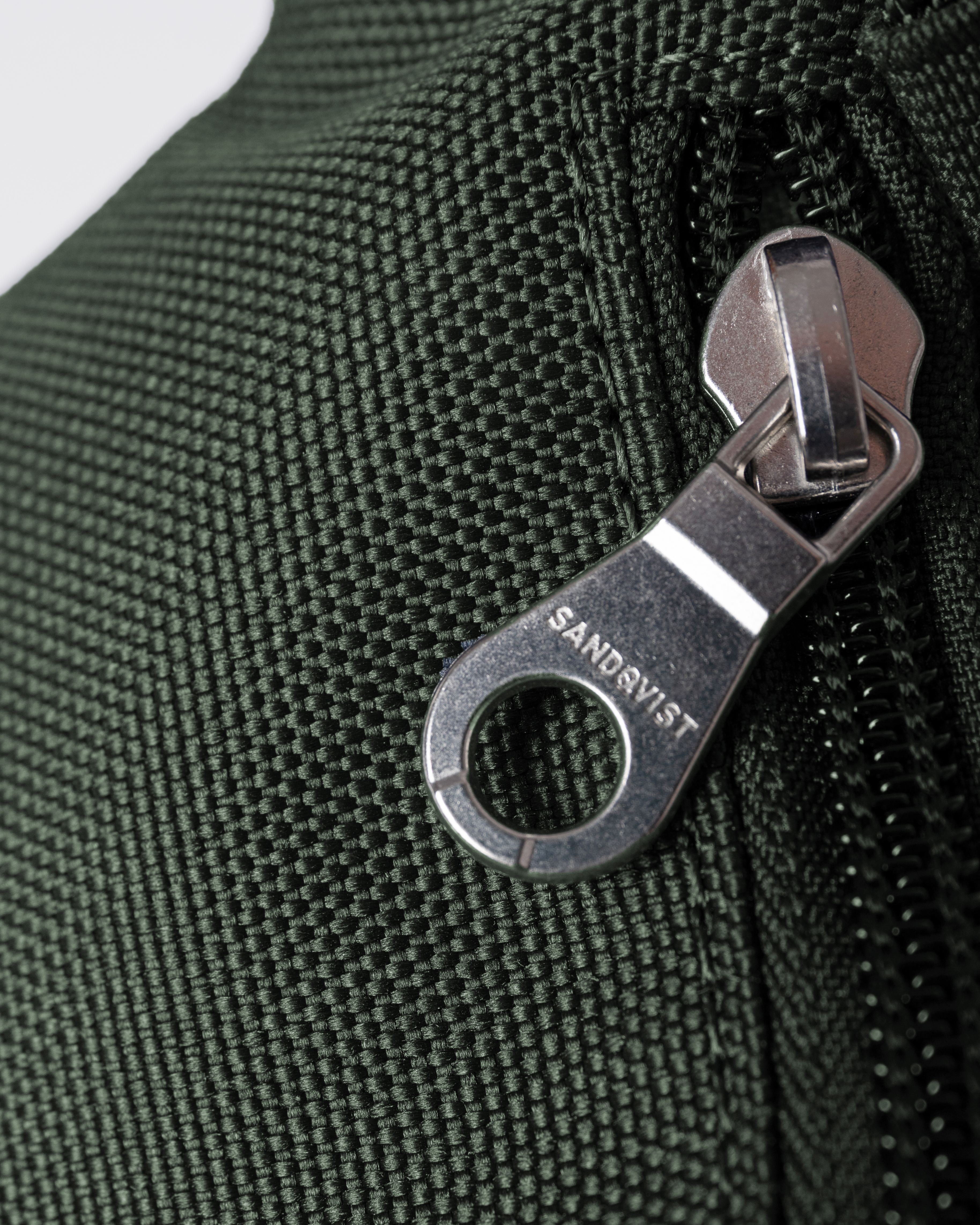 Sandqvist Ground Crossbody Bag, green. Close-up of zipper-puller.