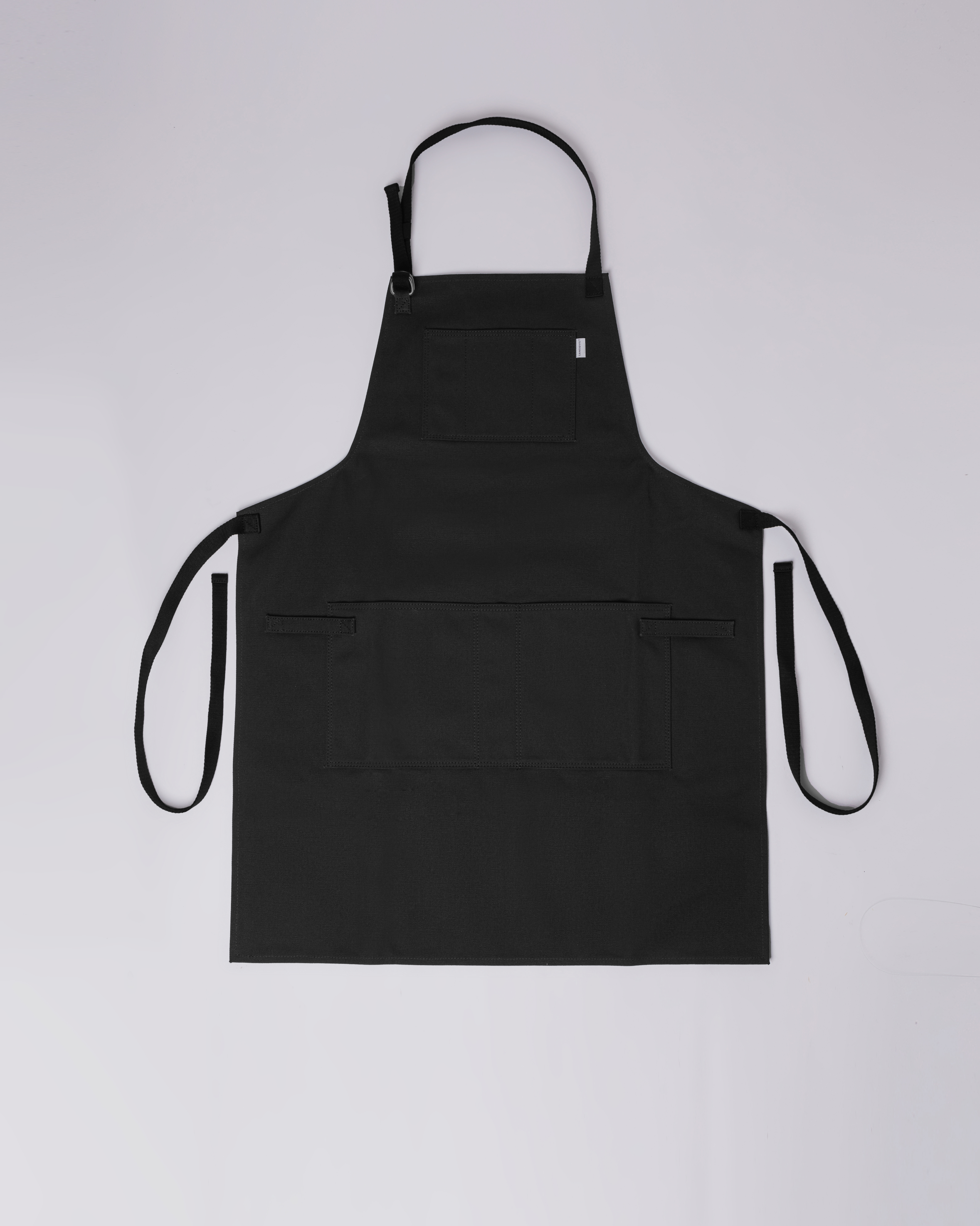 Apron. Sandqvist Apron in Black, front view with neck band, waist band and two pockets. 