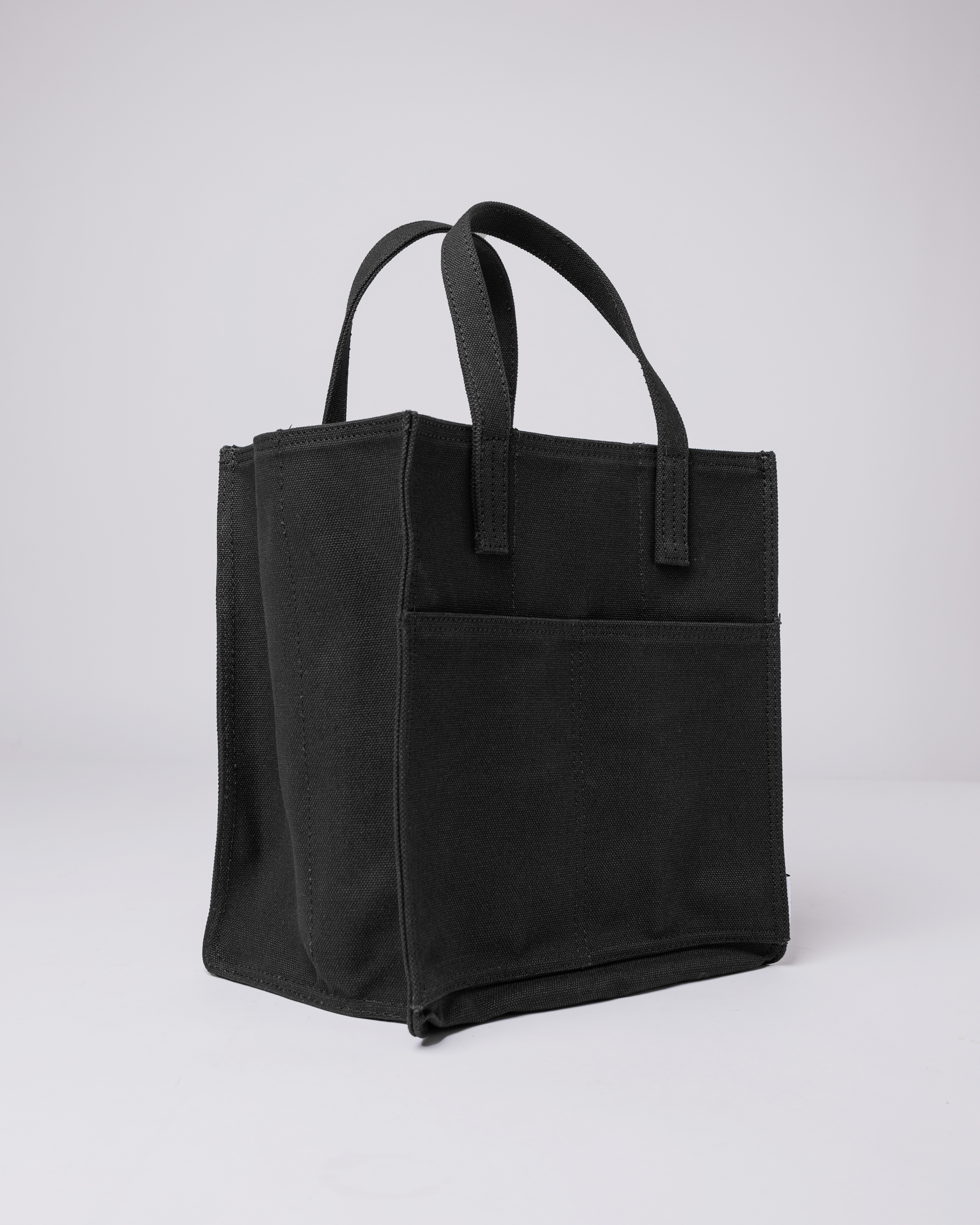 Sandqvist Bottle Bag in Black, side view with top handles and front slip pocket. 