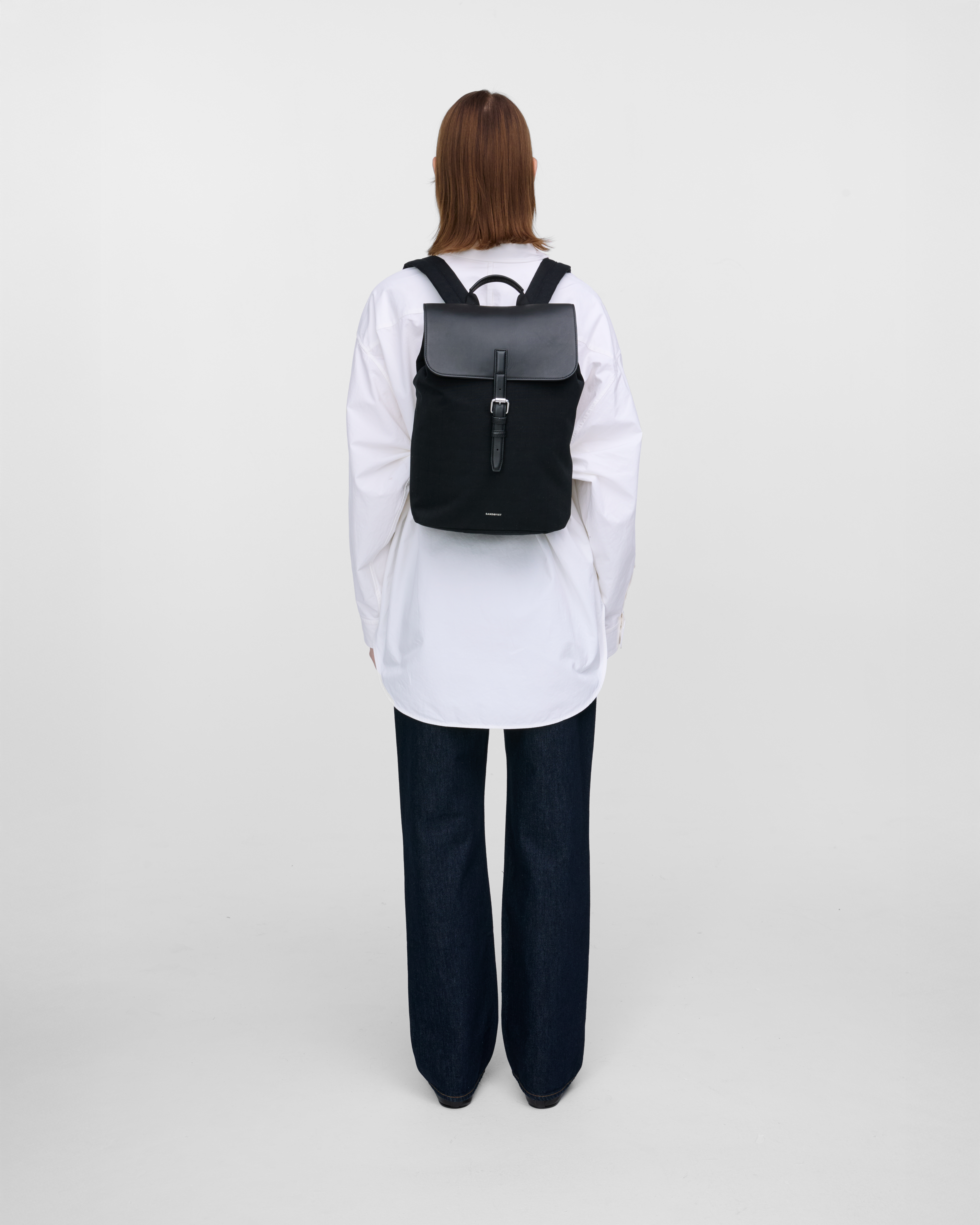 Female model wearing Sandqvist Everyday Lid Backpack M, black. Back view, wearing the bag in the back.