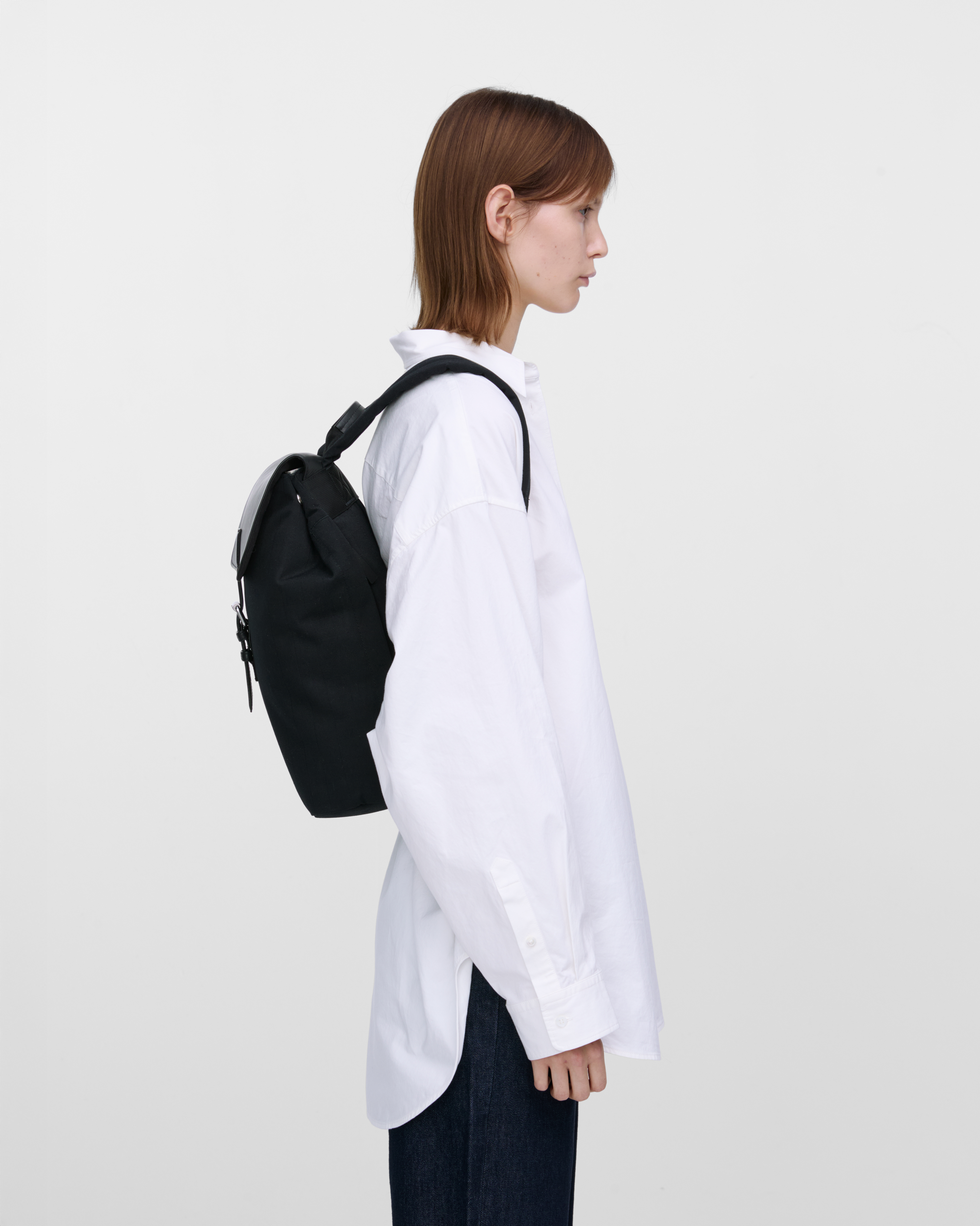 Female model wearing Sandqvist Everyday Lid Backpack M, black. Side view, wearing the bag on the back.