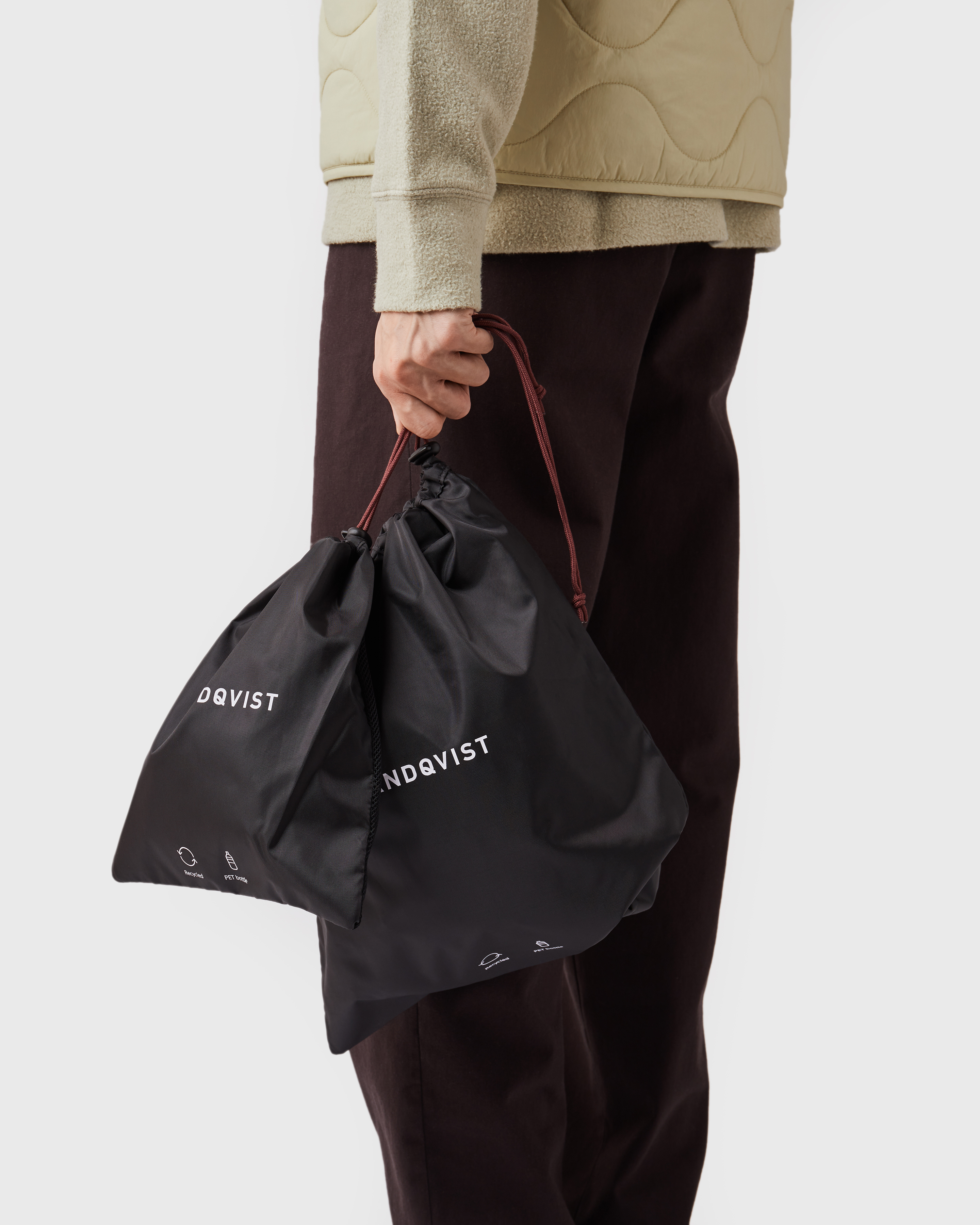 Male model holding two black pack bags in his hand. Side view showing size of Sandqvist ITEMS 3 Pack Bags.