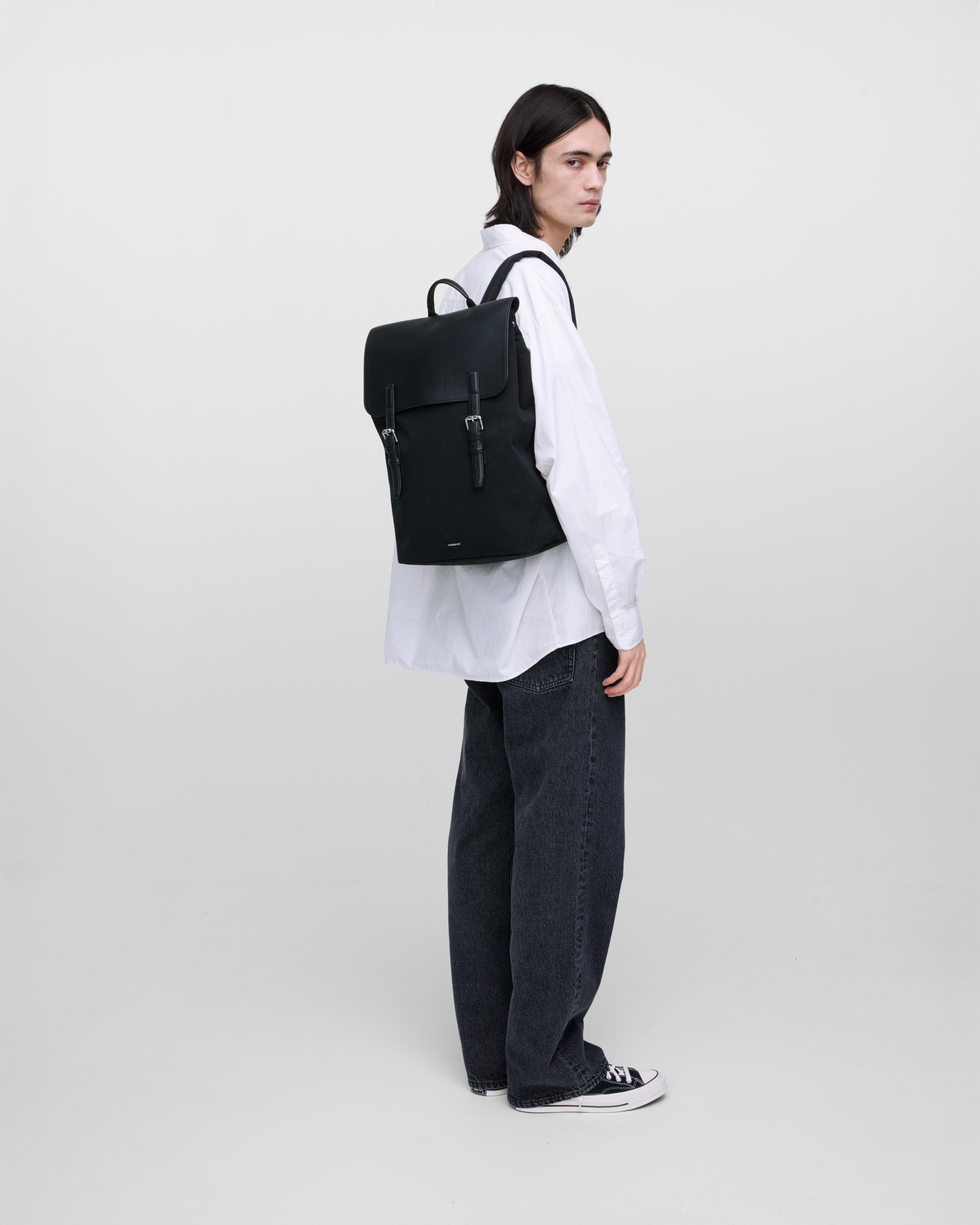 Male model wearing Sandqvist Everyday Lid Backpack L, black. Back view, wearing the bag on one shoulder on the back.