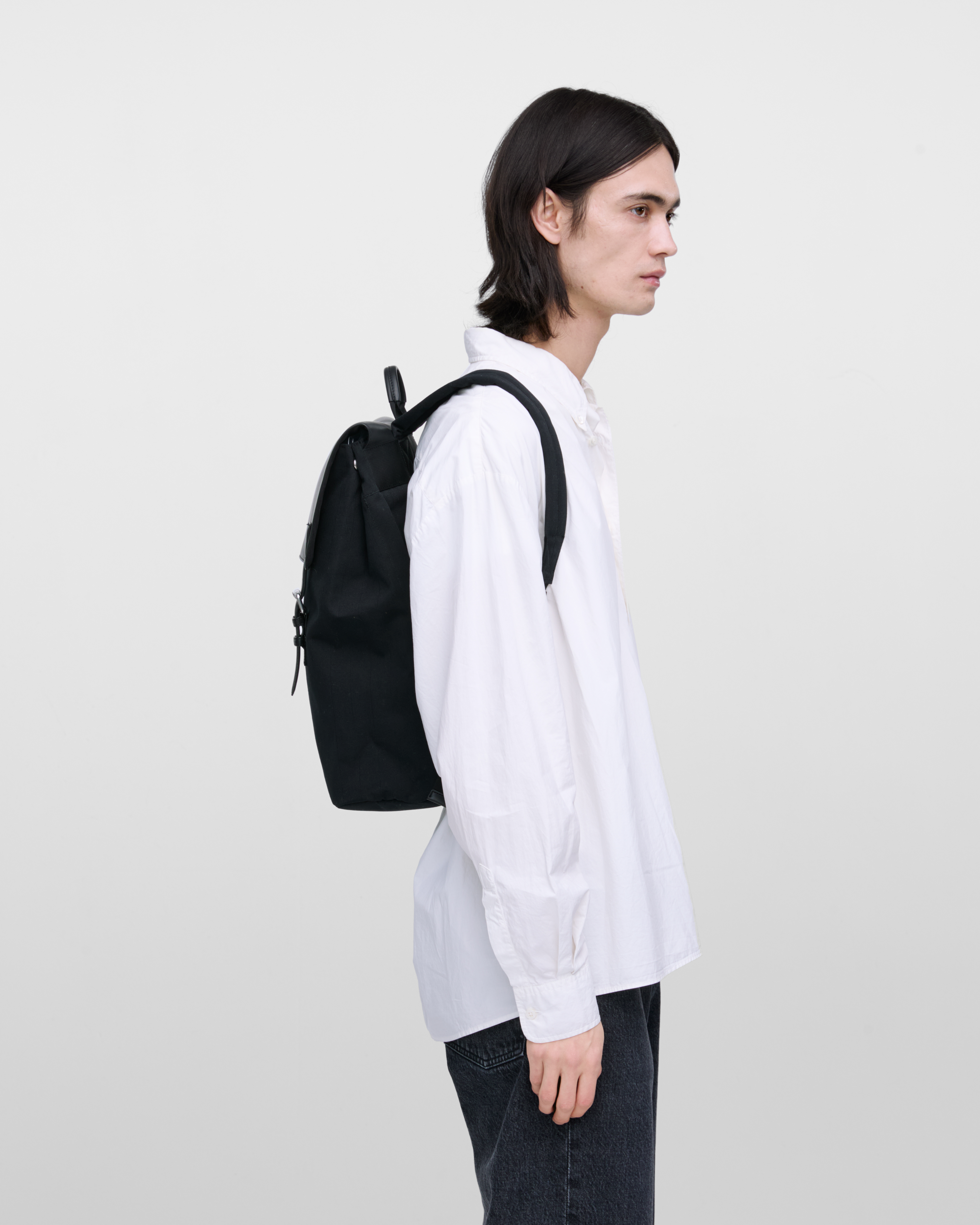 Male model wearing Sandqvist Everyday Lid Backpack, black. Side view, wearing the bag on the back.