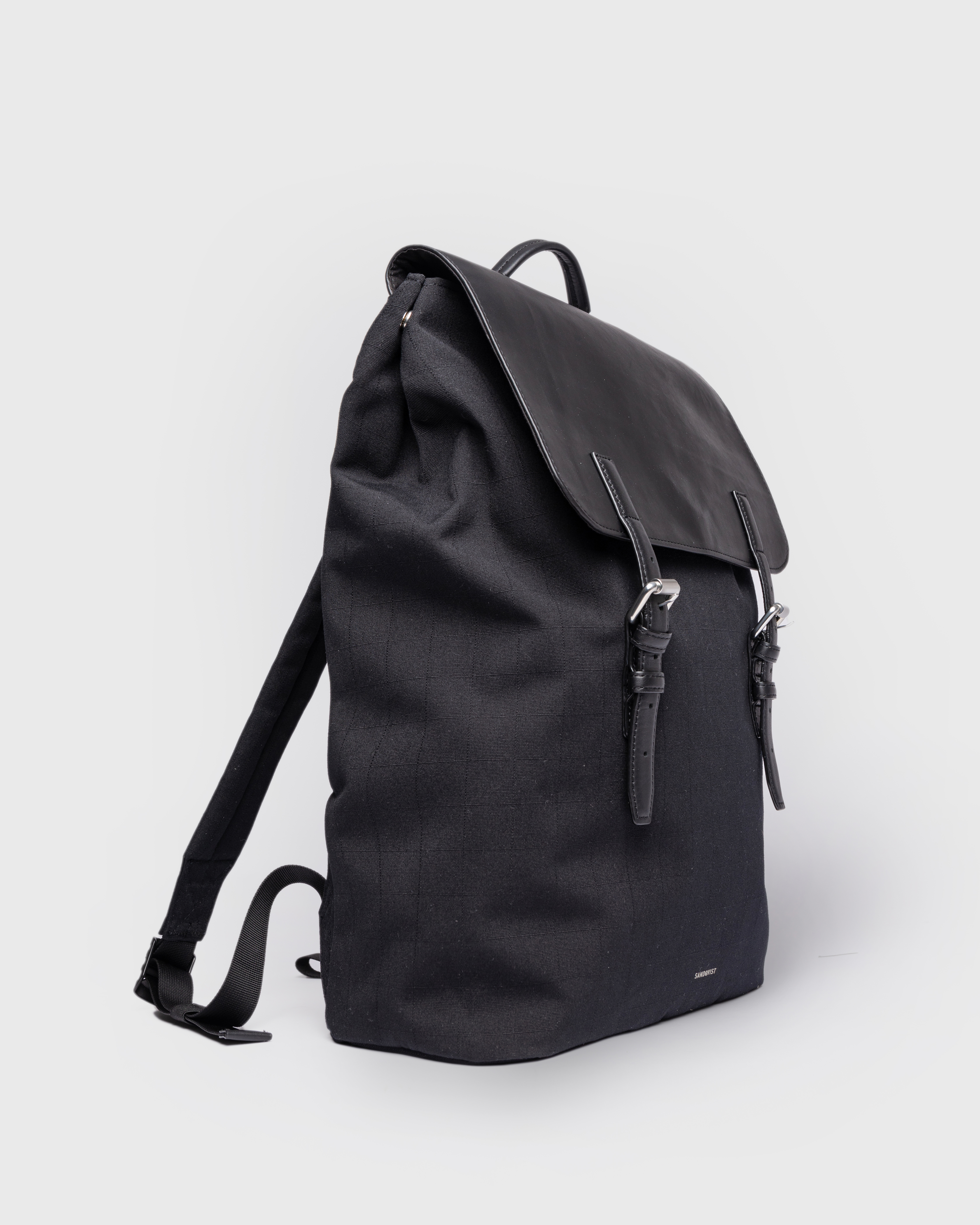 Sandqvist Everyday Lid Backpack, black. Side view, lid with two buckles, one handle and shoulder straps.