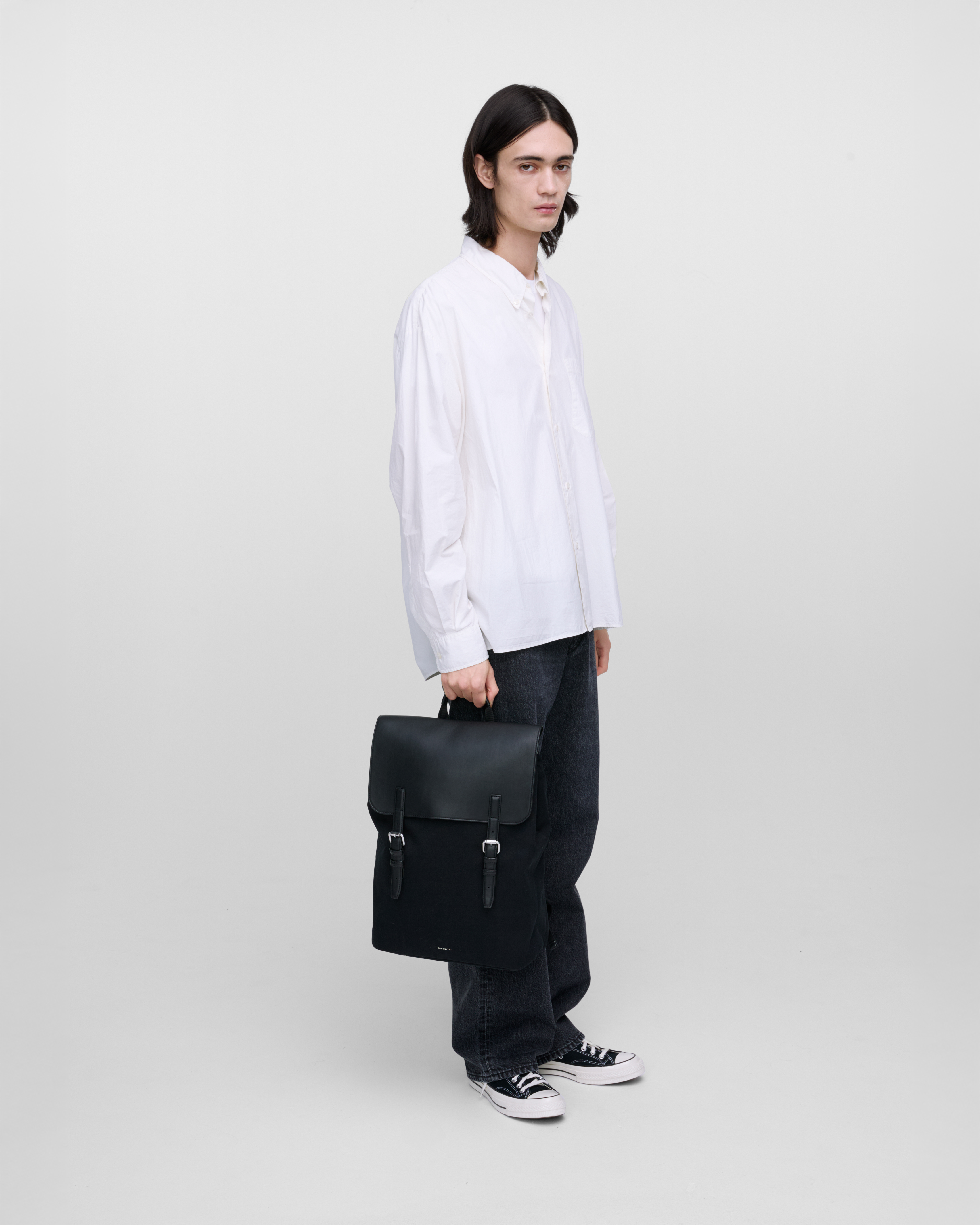 Male model holding Sandqvist Everyday Lid Backpack L, black. Side view, holding the bag in one hand.