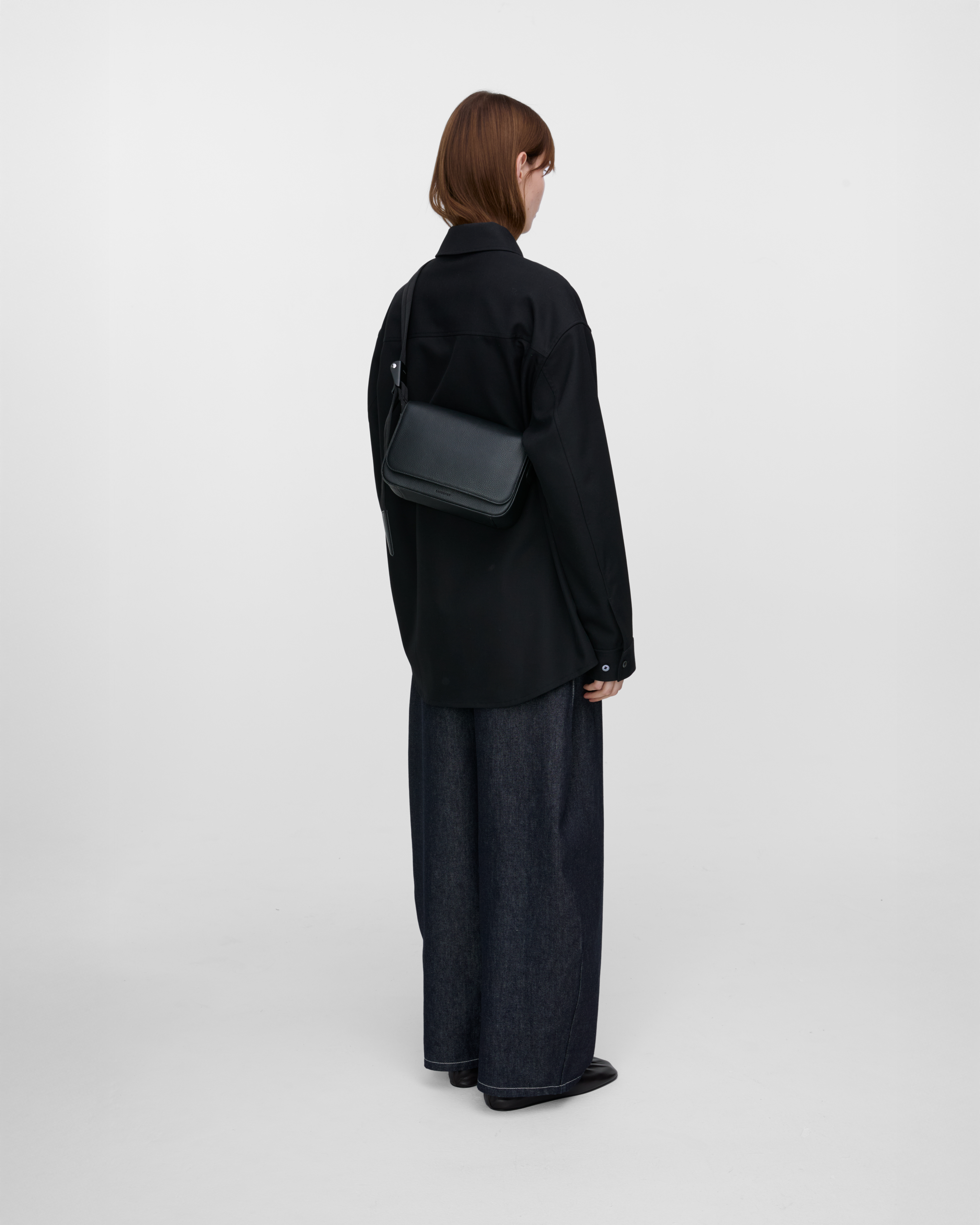 Female model carrying Sandqvist Agile Crossbody Bag, black. Back view, carrying the bag crossbody with the bag on the back.