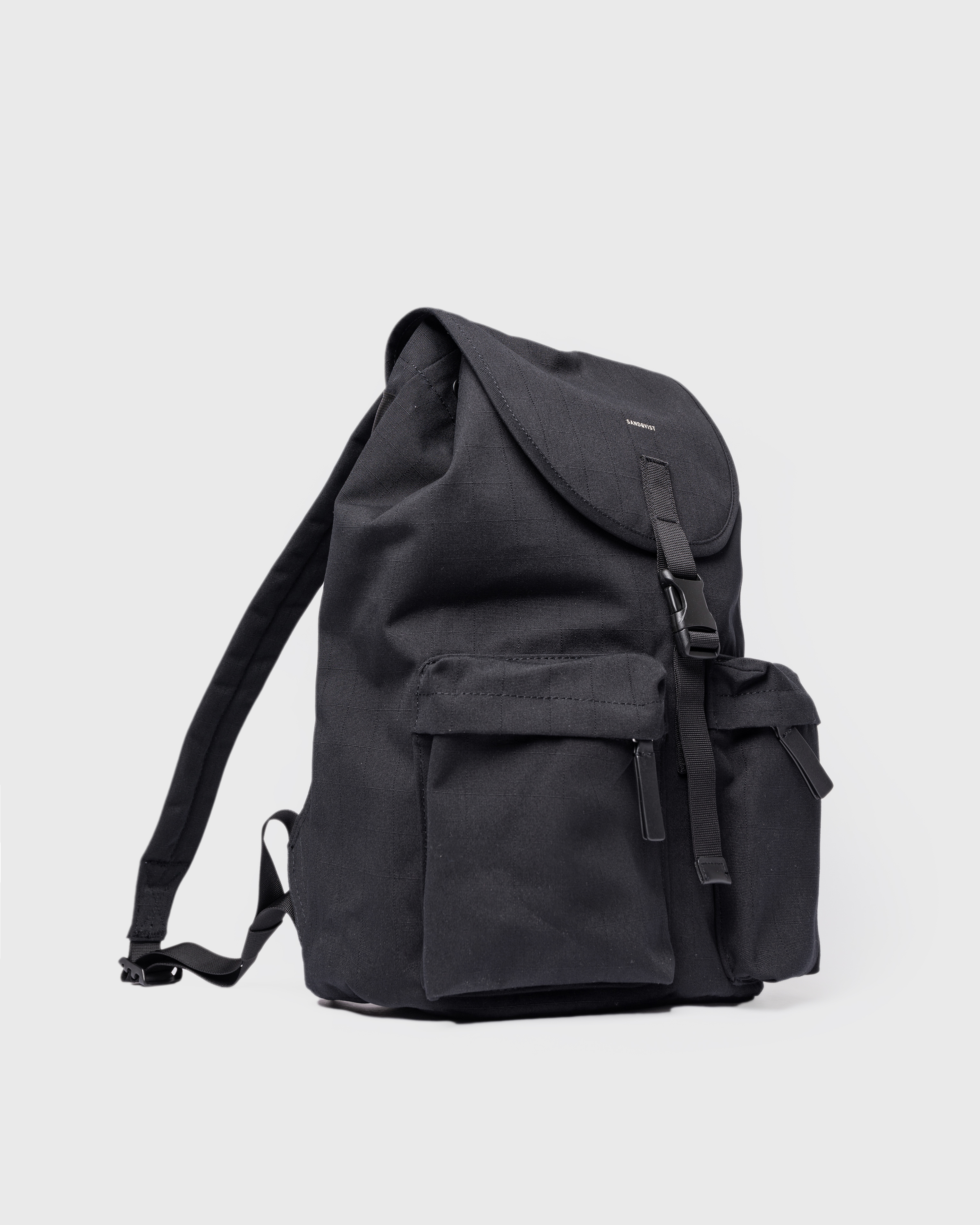 Sandqvist Everyday Rucksack, black. Side view, lid with buckle, two pockets with zippers and shoulder strap.