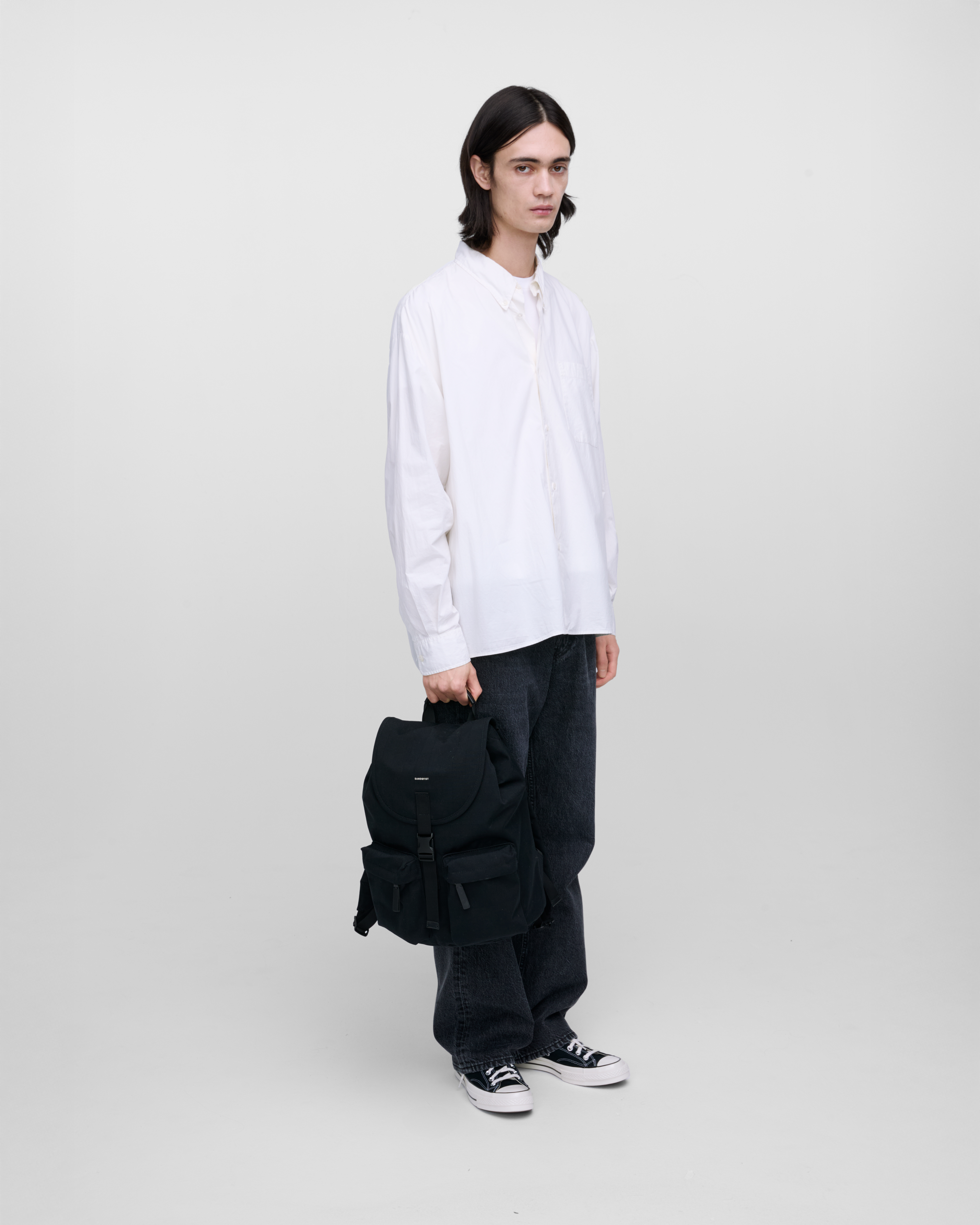 Male model holding Sandqvist Everyday Rucksack, black. Front view, holding the bag in one hand.