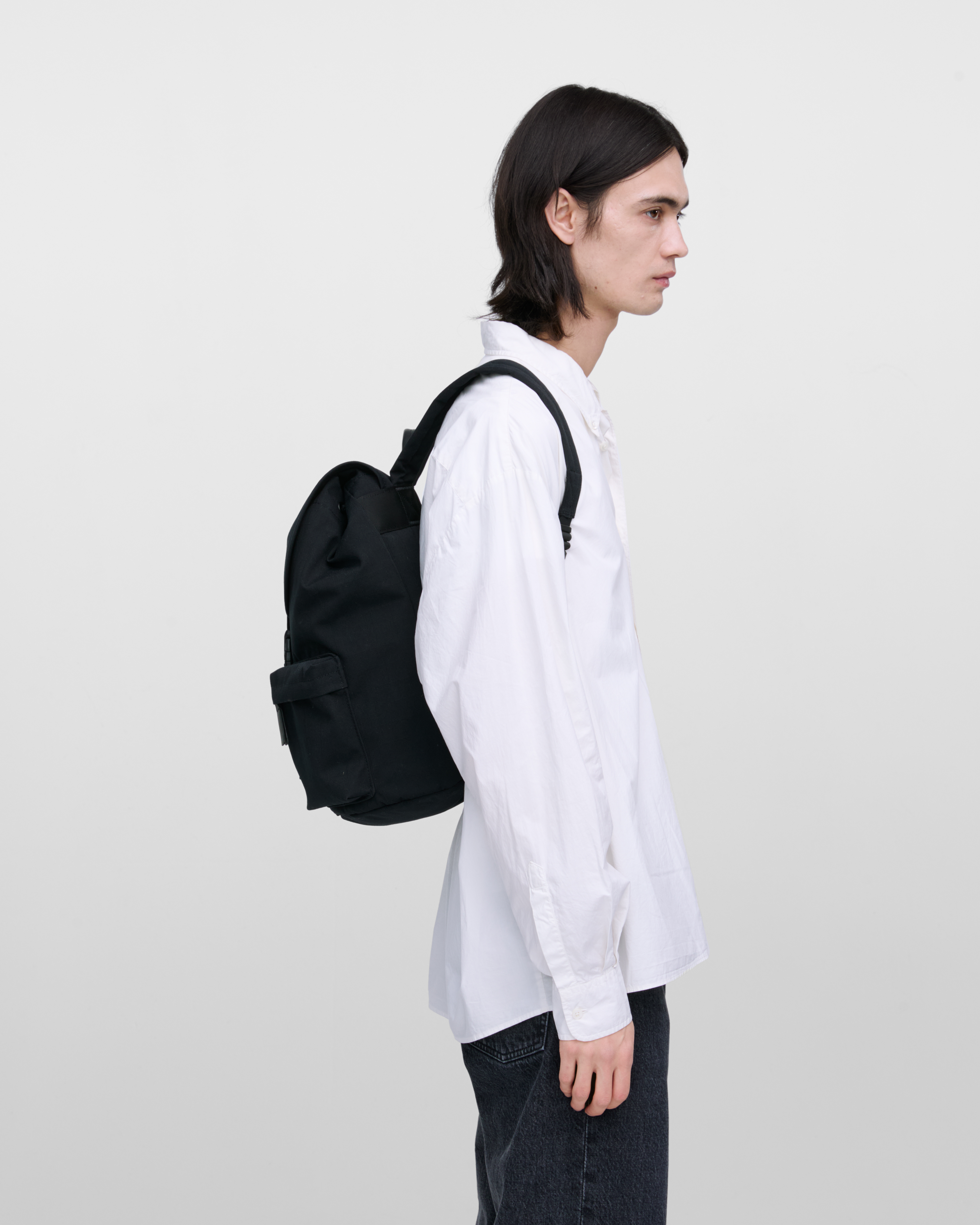 Male model wearing Sandqvist Everyday Rucksack, black. Side view, wearing the bag on the back.
