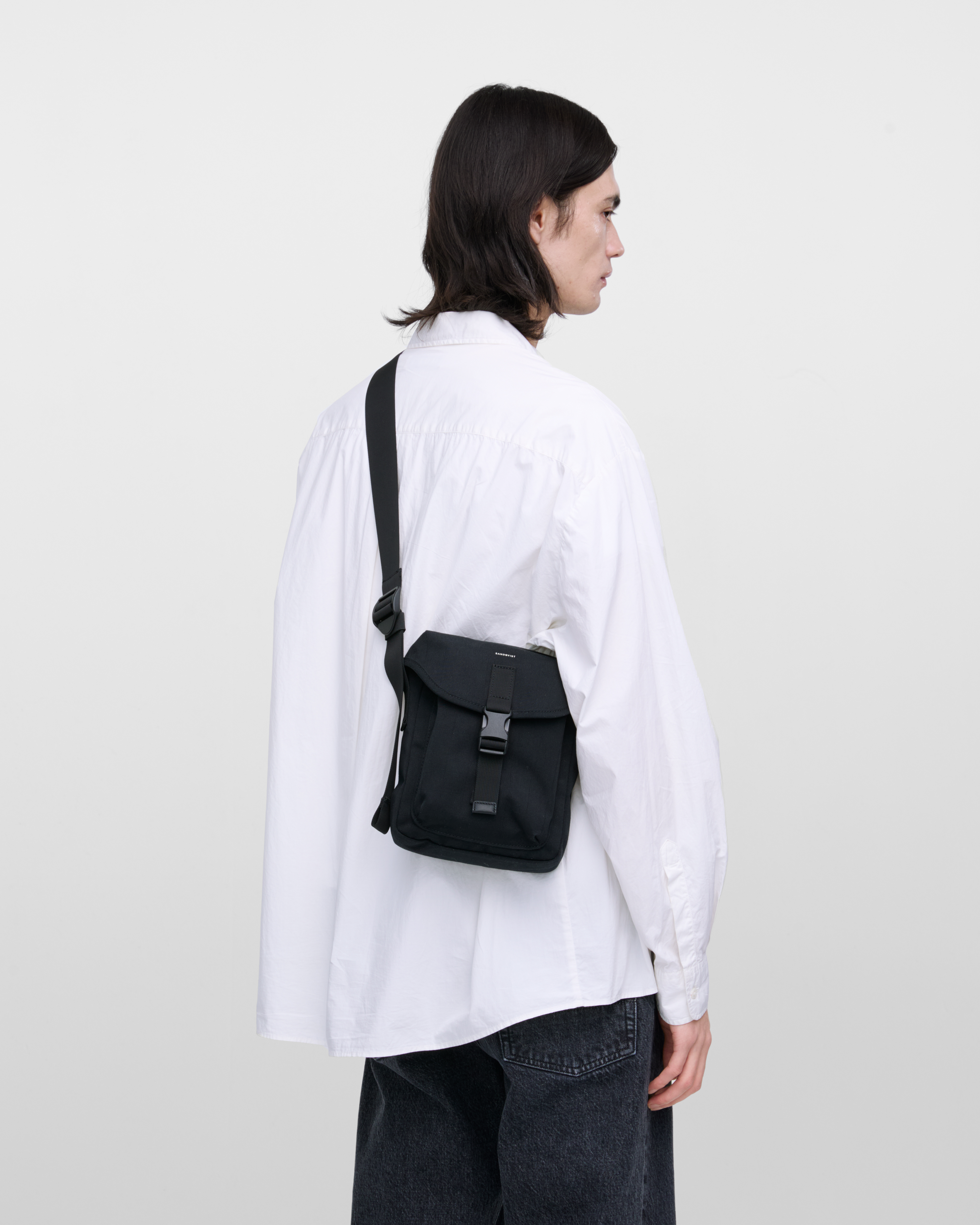 Male model wearing Sandqvist Everyday crossbody bag, black. Back view, wearing the bag on one shoulder crossbody, with the bag in the back.