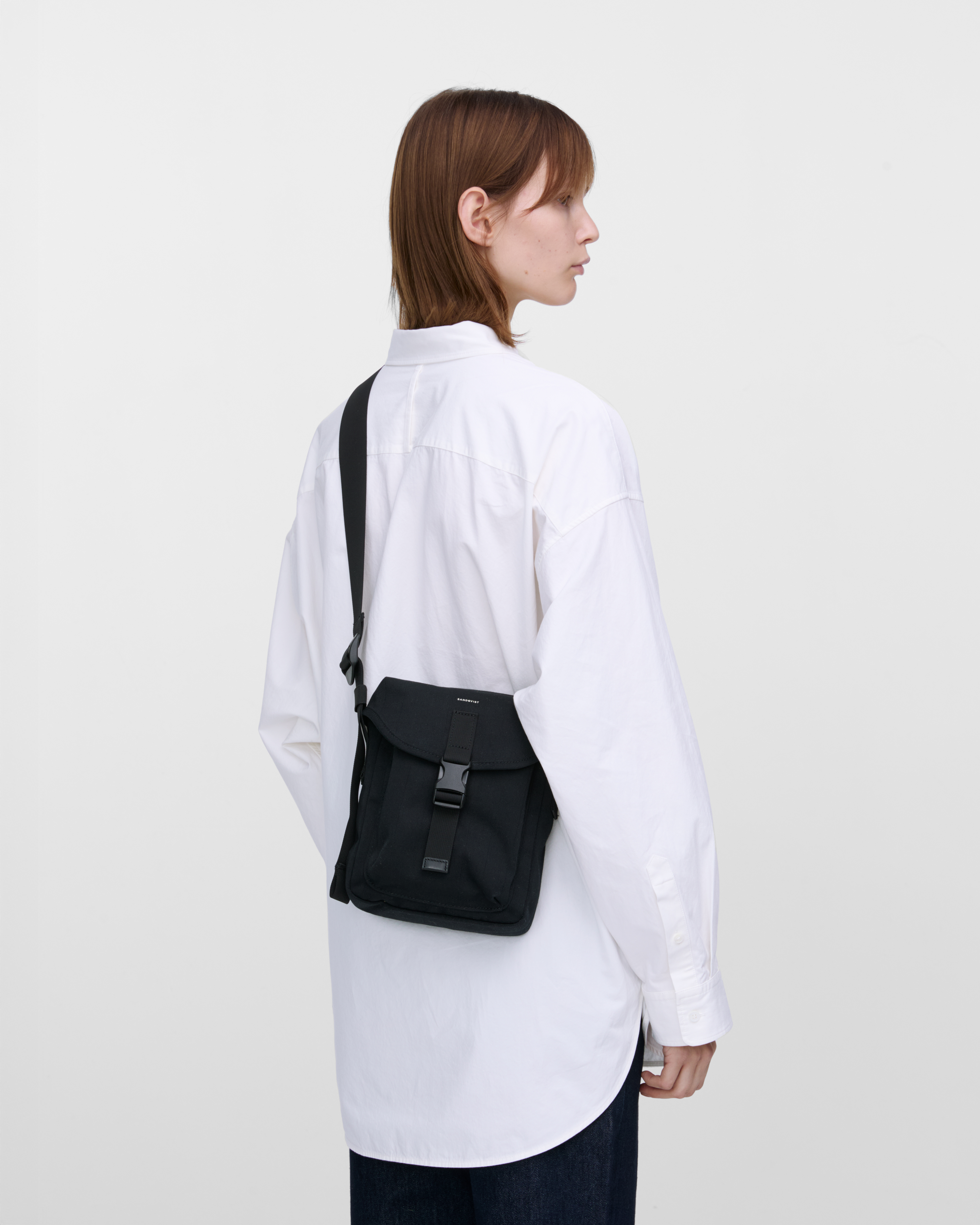 Female model wearing Sandqvist Everyday crossbody bag, black. Back view, wearing the bag on one shoulder crossbody, with the bag in the back.