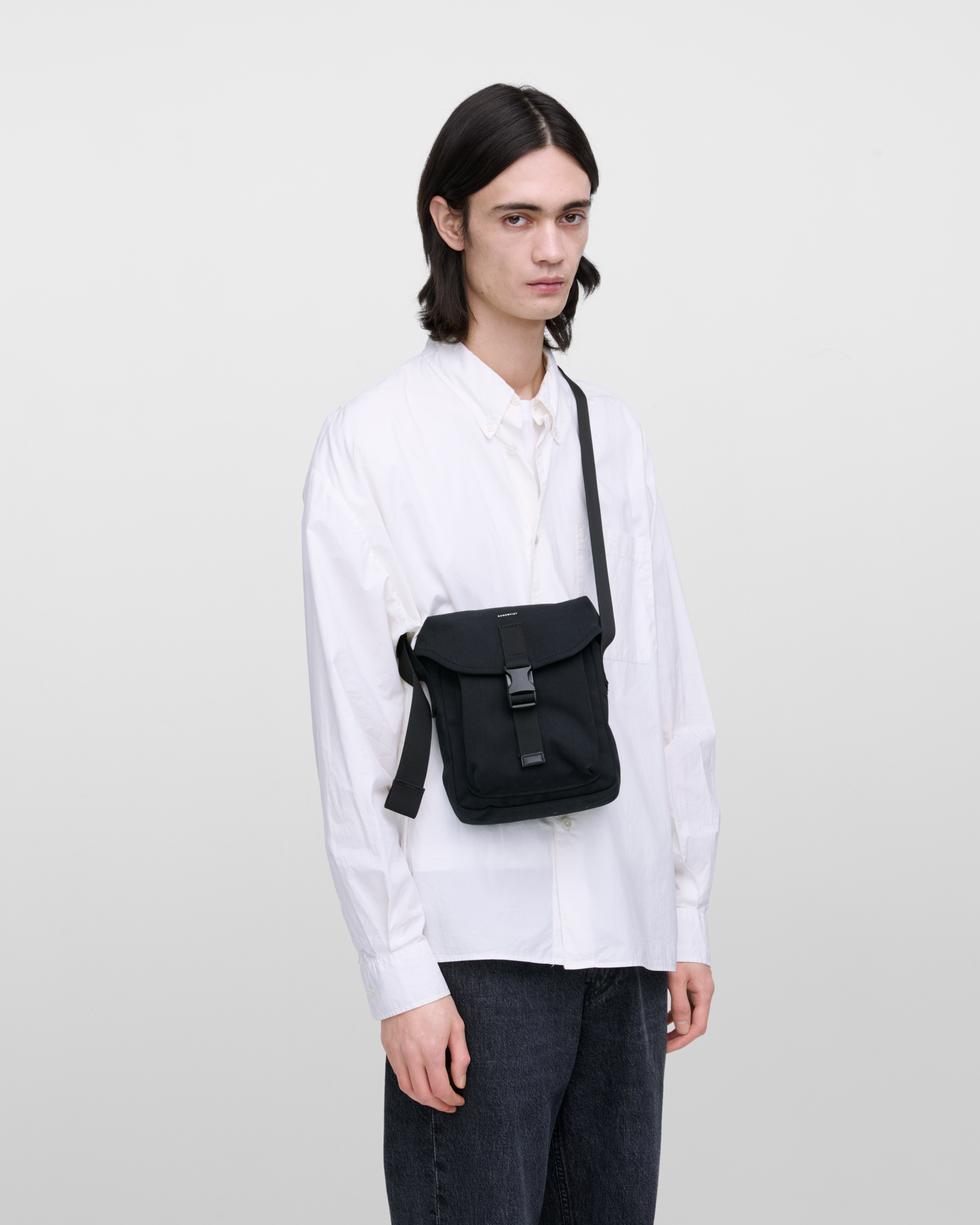 Male model wearing Sandqvist Everyday crossbody bag, black. Front view, wearing the bag on one shoulder crossbody, with the bag in the front.