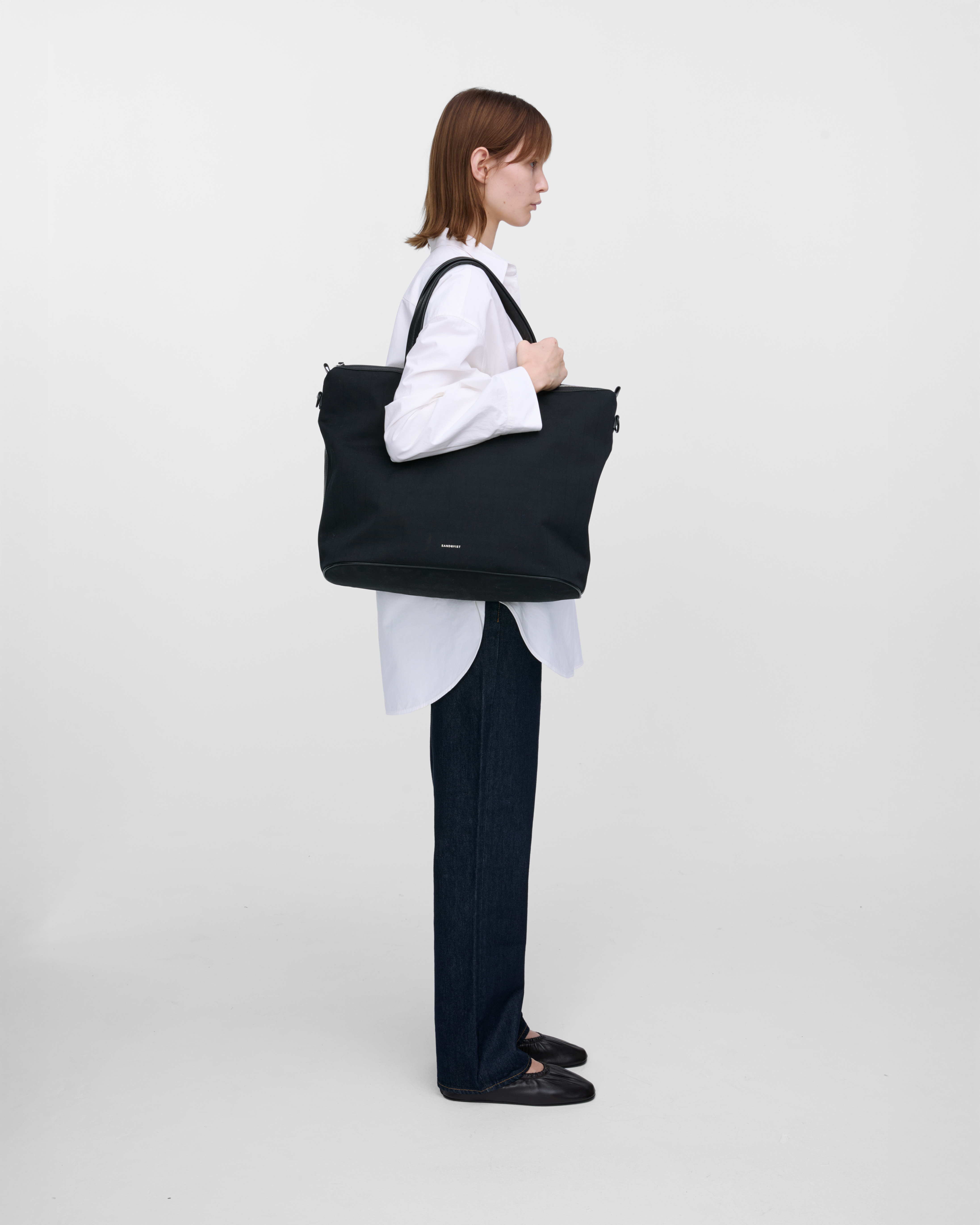 Female model wearing Sandqvist Everyday Weekend Bag, black. Side view, wearing the bag on one shoulder.