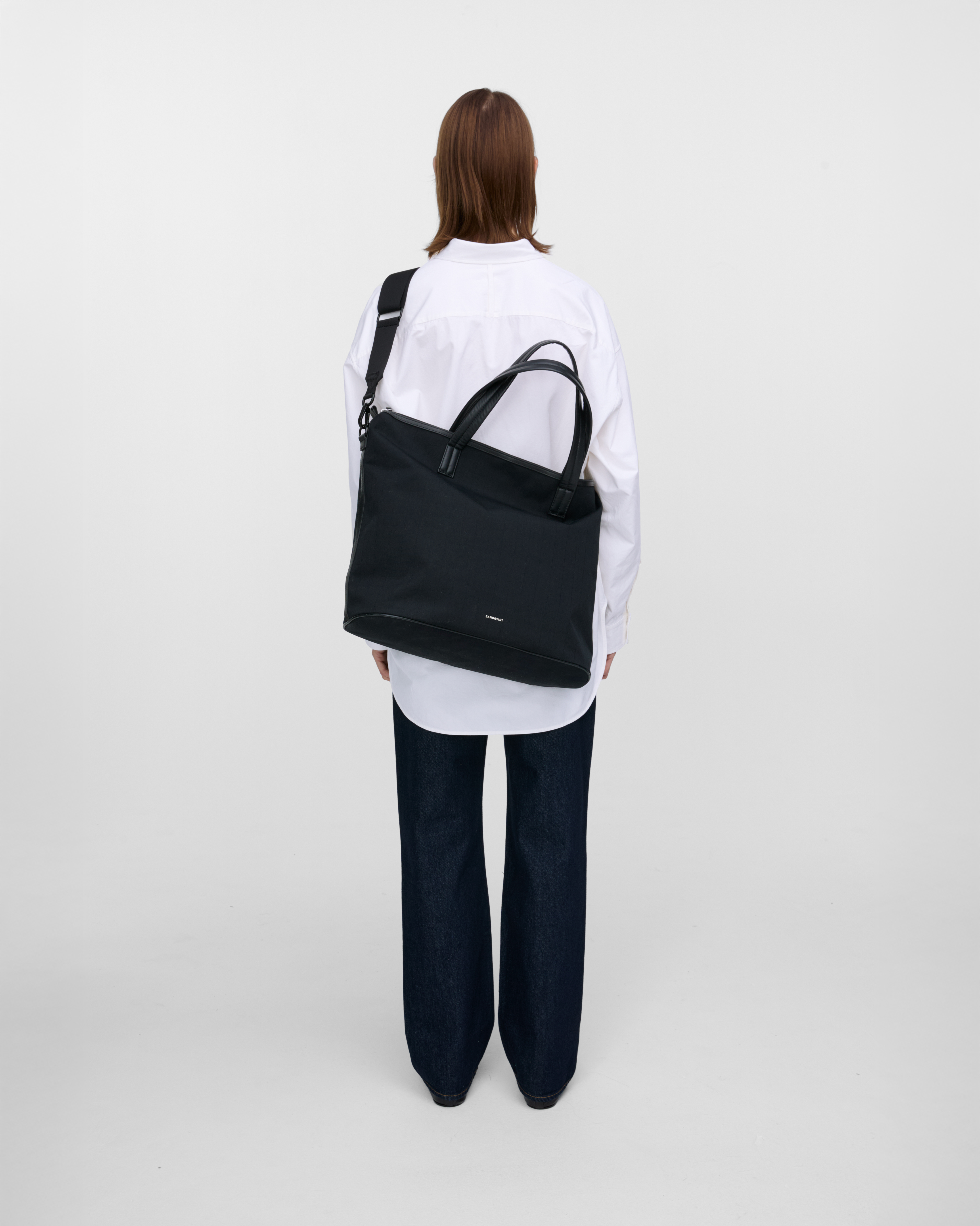 Female model wearing Sandqvist Everyday Weekend Bag, black. Back view, wearing the bag on one shoulder crossbody with the bag on the back.